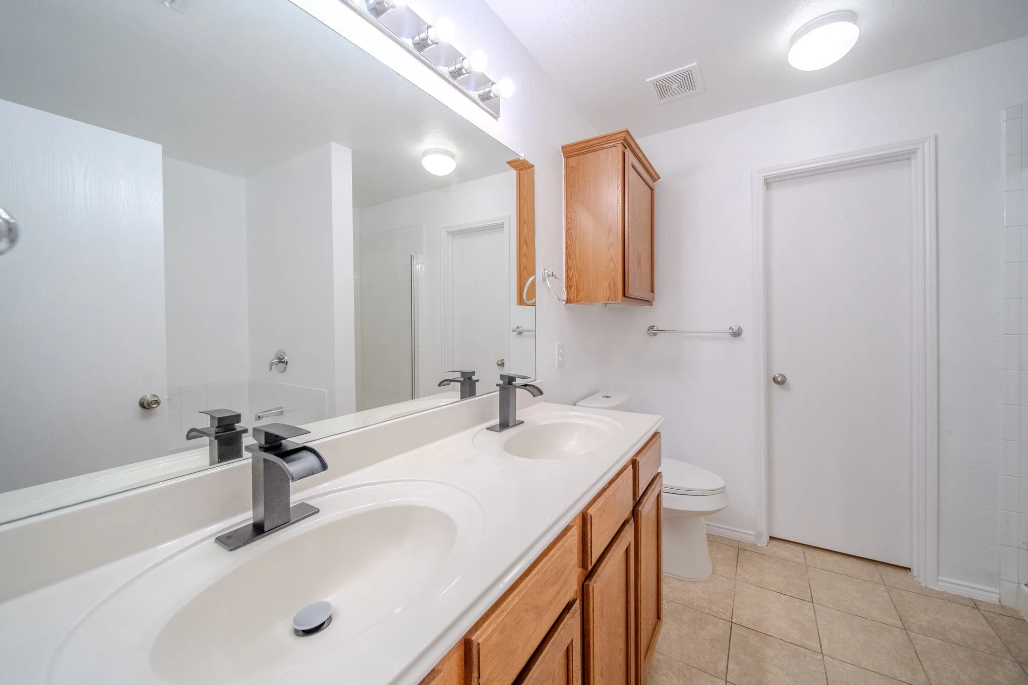 Bathroom featuring a dual vanity with integrated sinks, contemporary black faucets, wood-finish cabinetry, and a full-width mirror