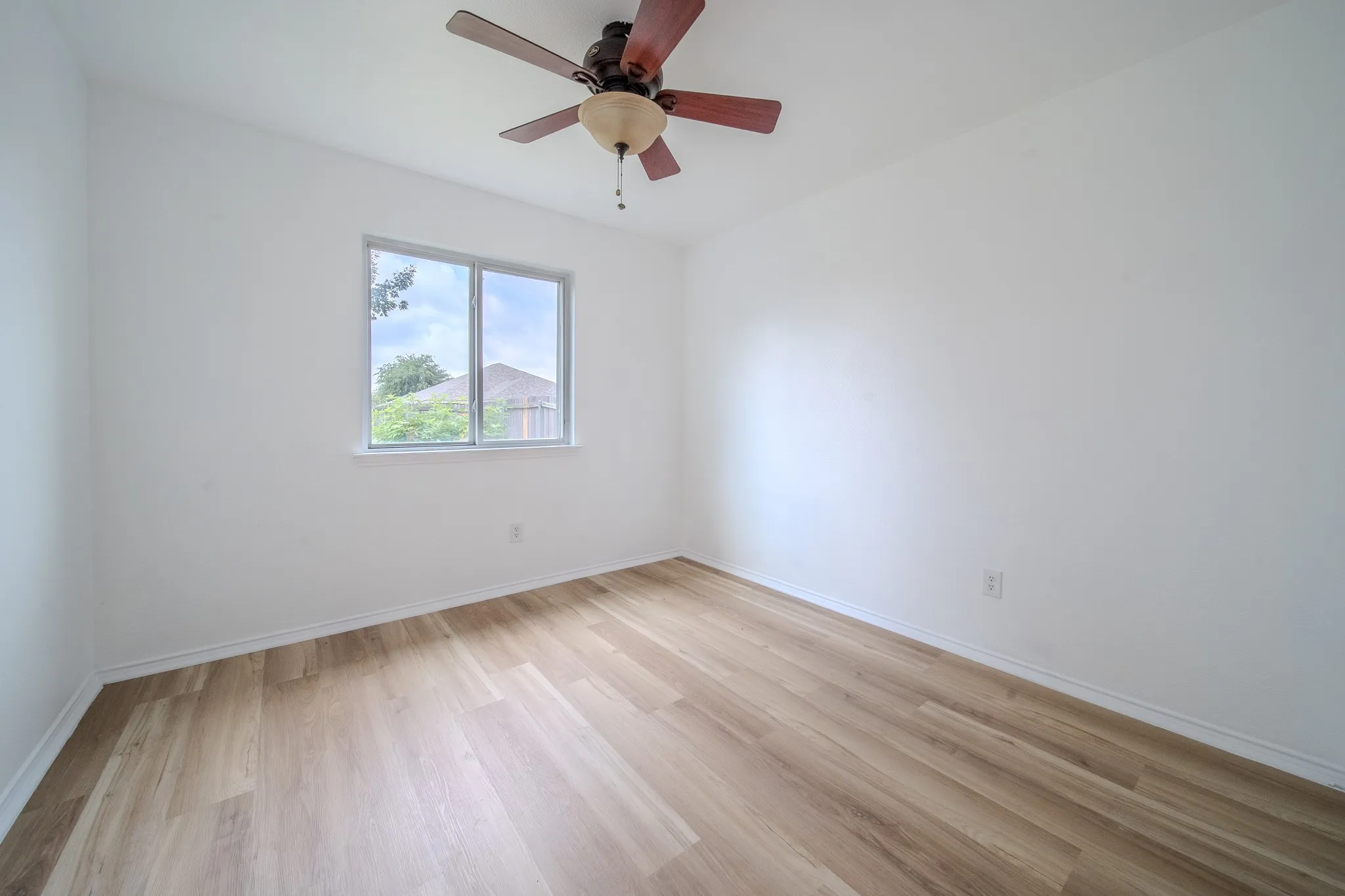 Bright room featuring wood-finish flooring, white walls, a multi-pane window, white trim, and a ceiling fan with light fixture