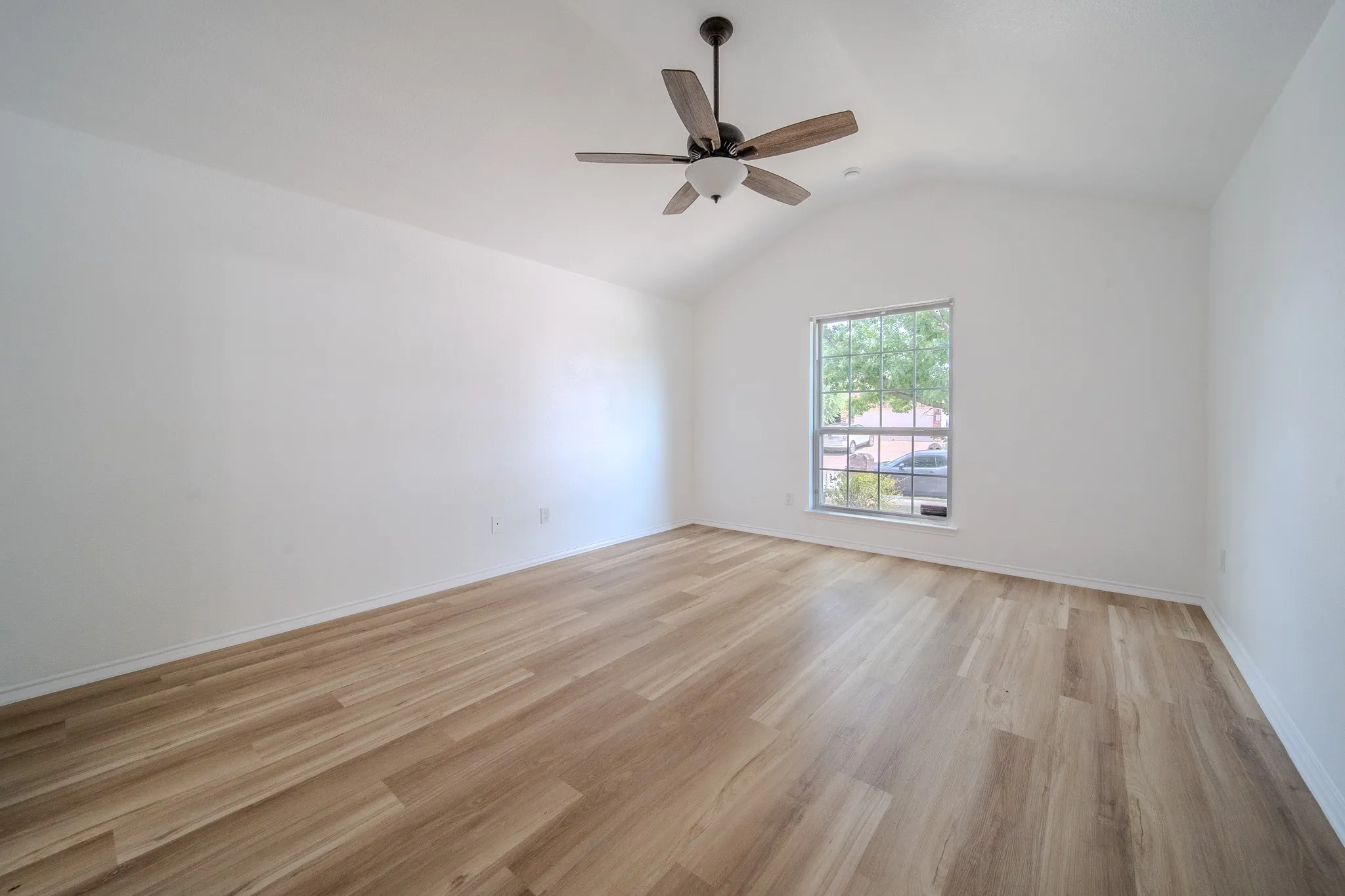 Spacious room featuring vaulted ceilings, wood-finish flooring, a ceiling fan with light kit, and a large window