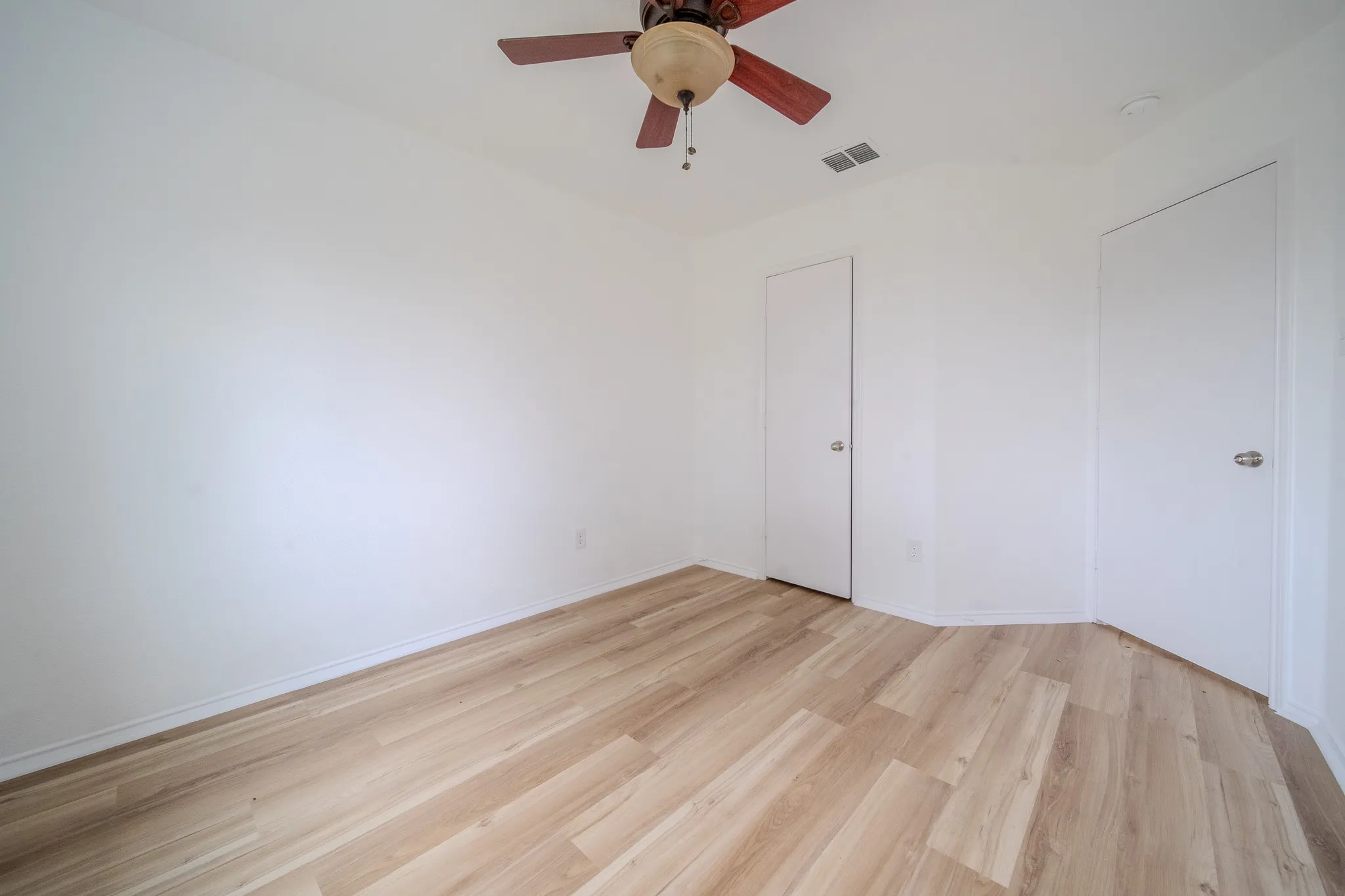 Room featuring wood-finish flooring, crisp white walls, and a ceiling fan with light fixture