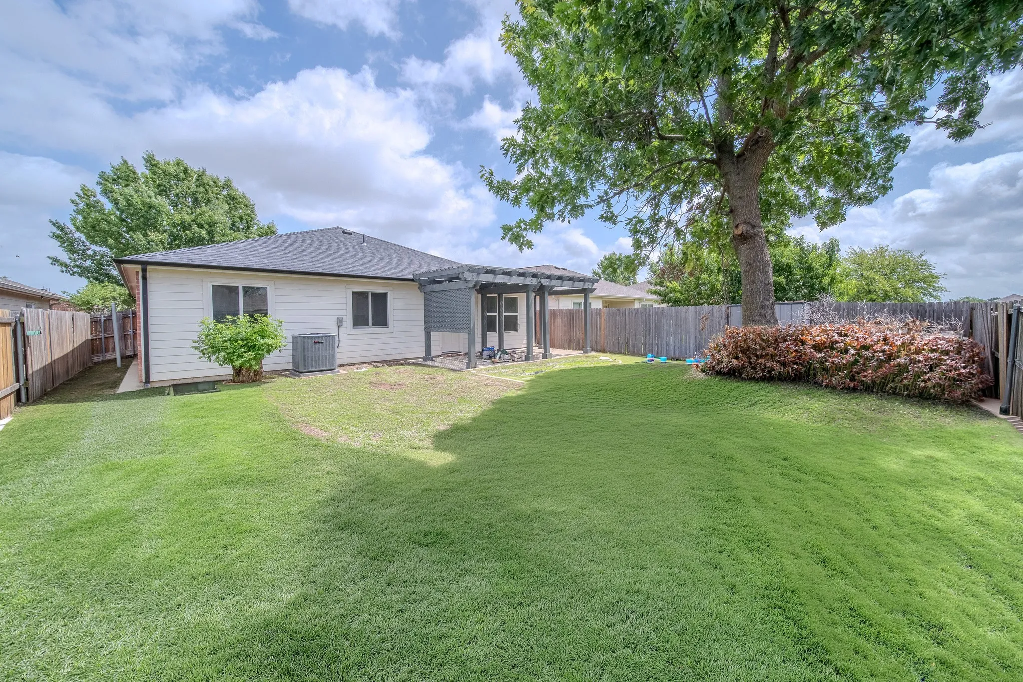 Expansive backyard featuring a large mature tree, established shrubbery, and a full privacy fence