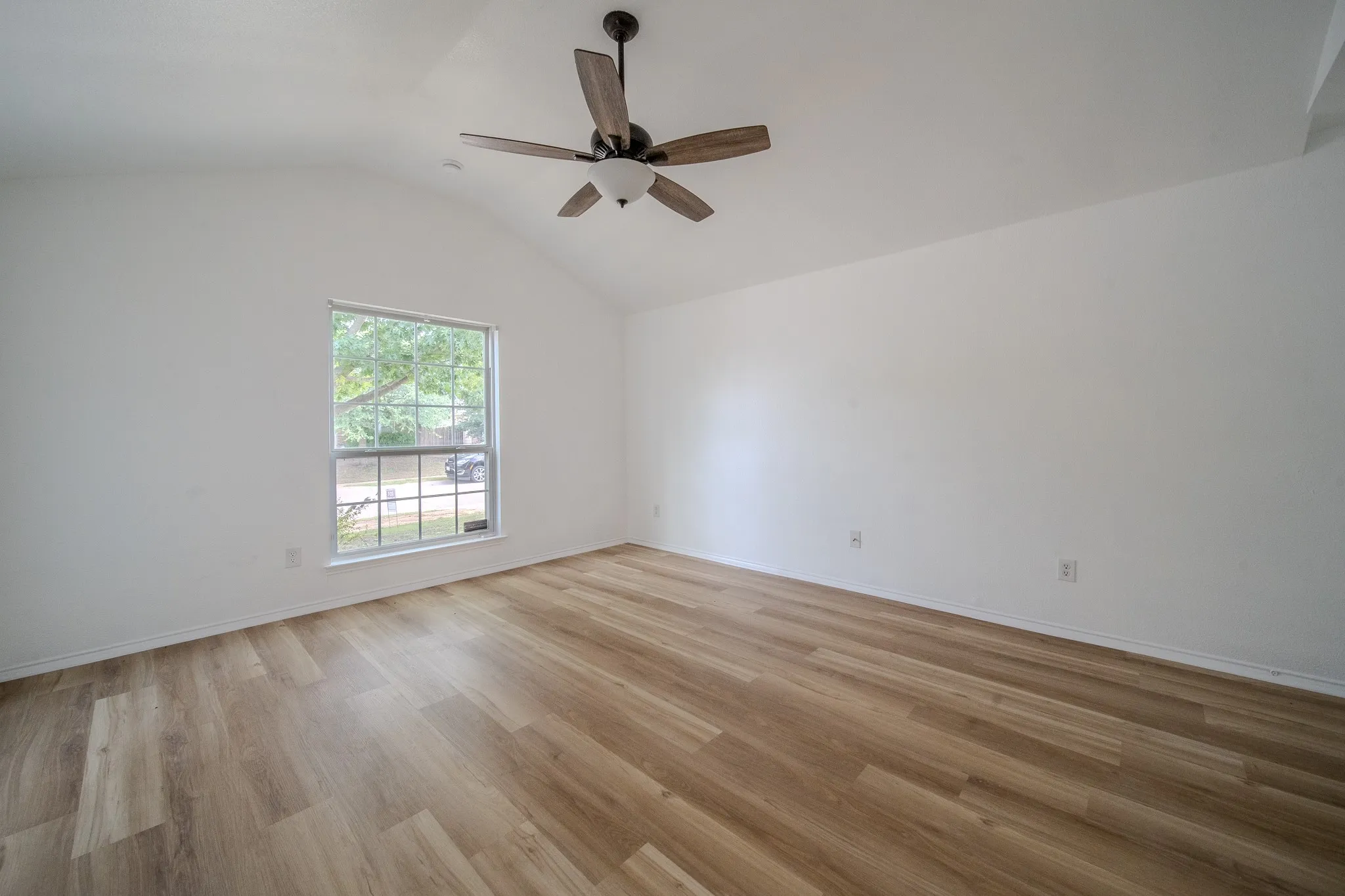 Spacious room featuring vaulted ceilings, a contemporary ceiling fan, and wood-finish flooring
