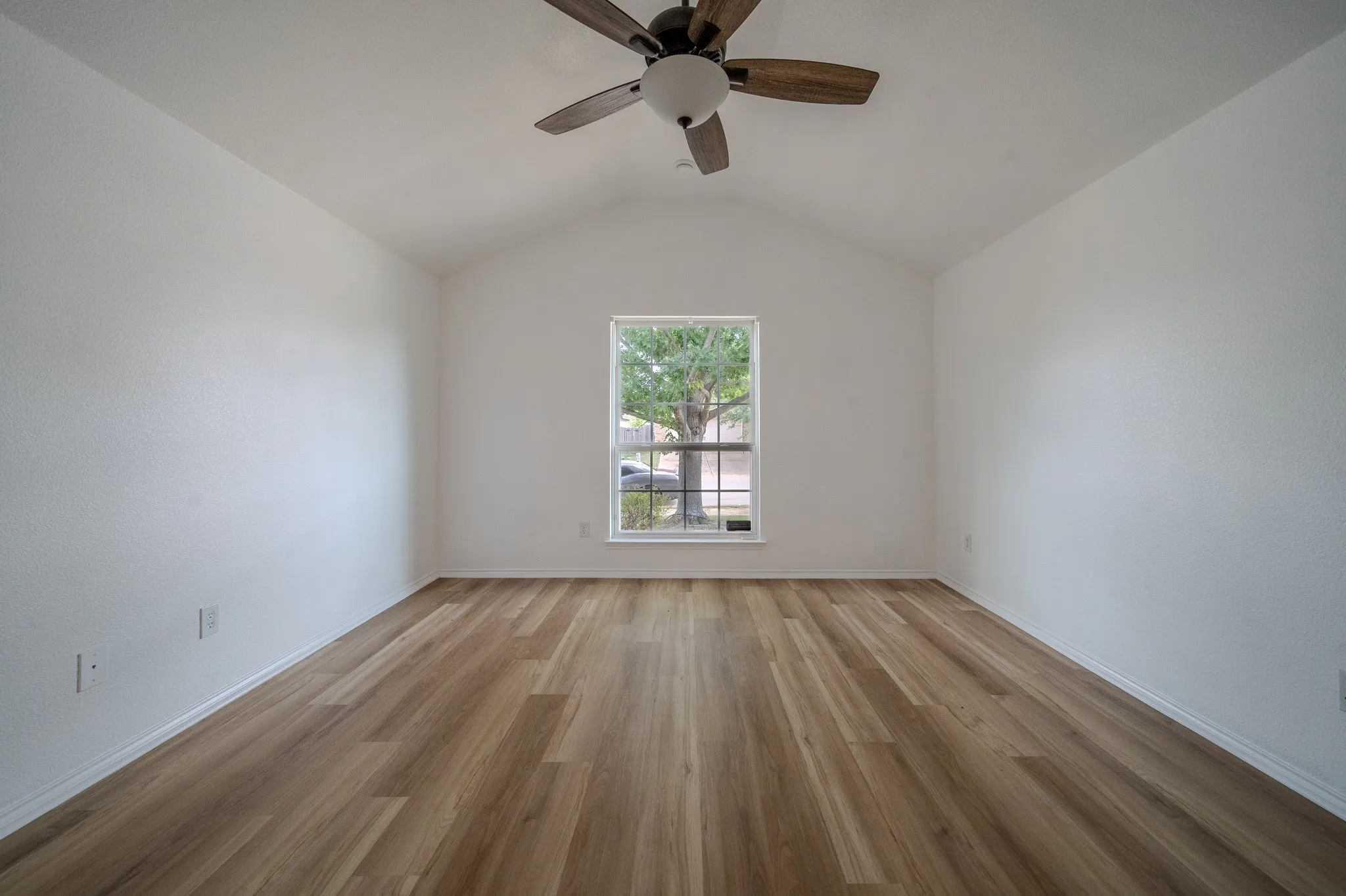 Vaulted ceiling room featuring wood-finish flooring, a ceiling fan with light, and a window with white trim