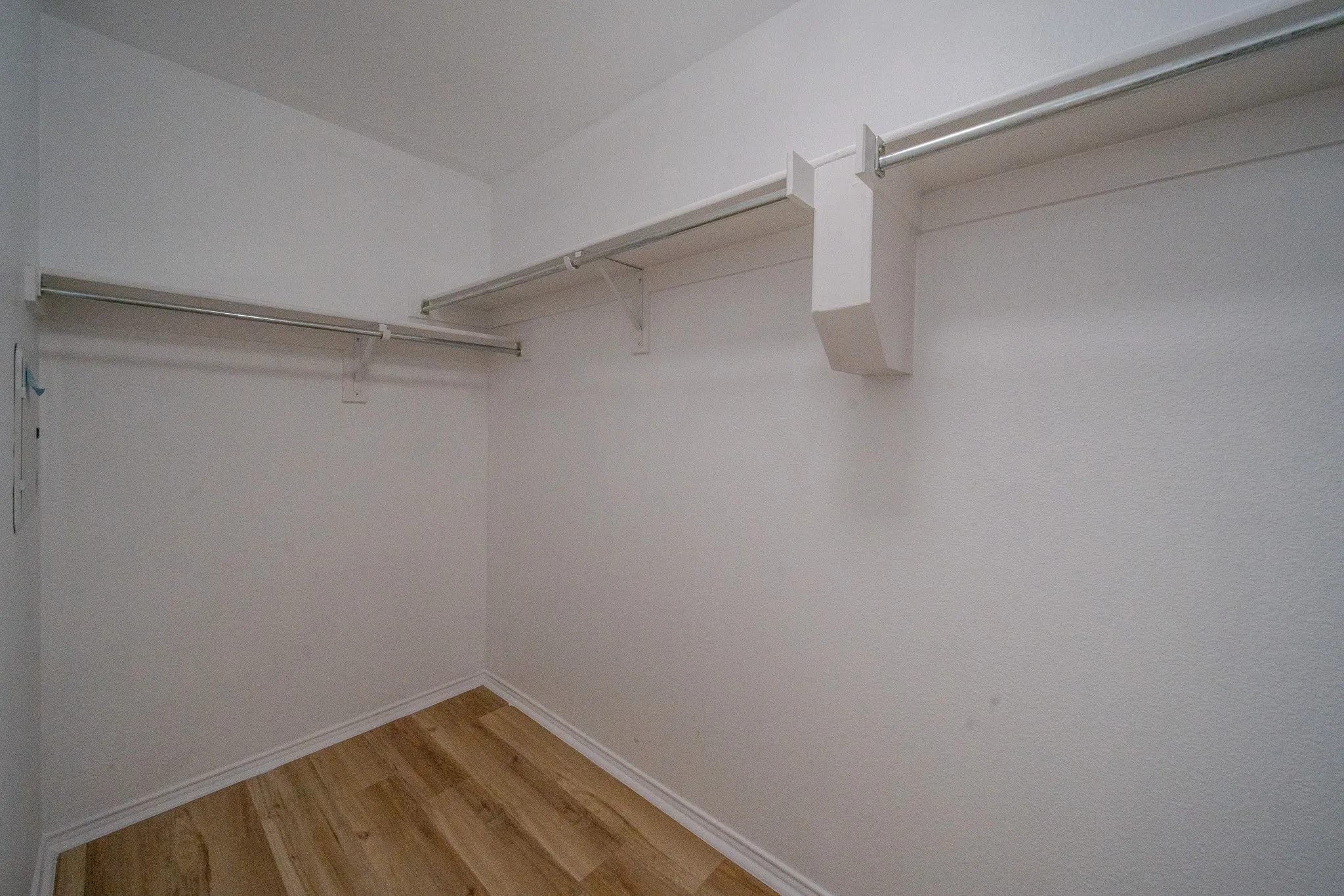 Walk-in closet featuring wood-finish flooring, white walls, and built-in shelving with hanging rods