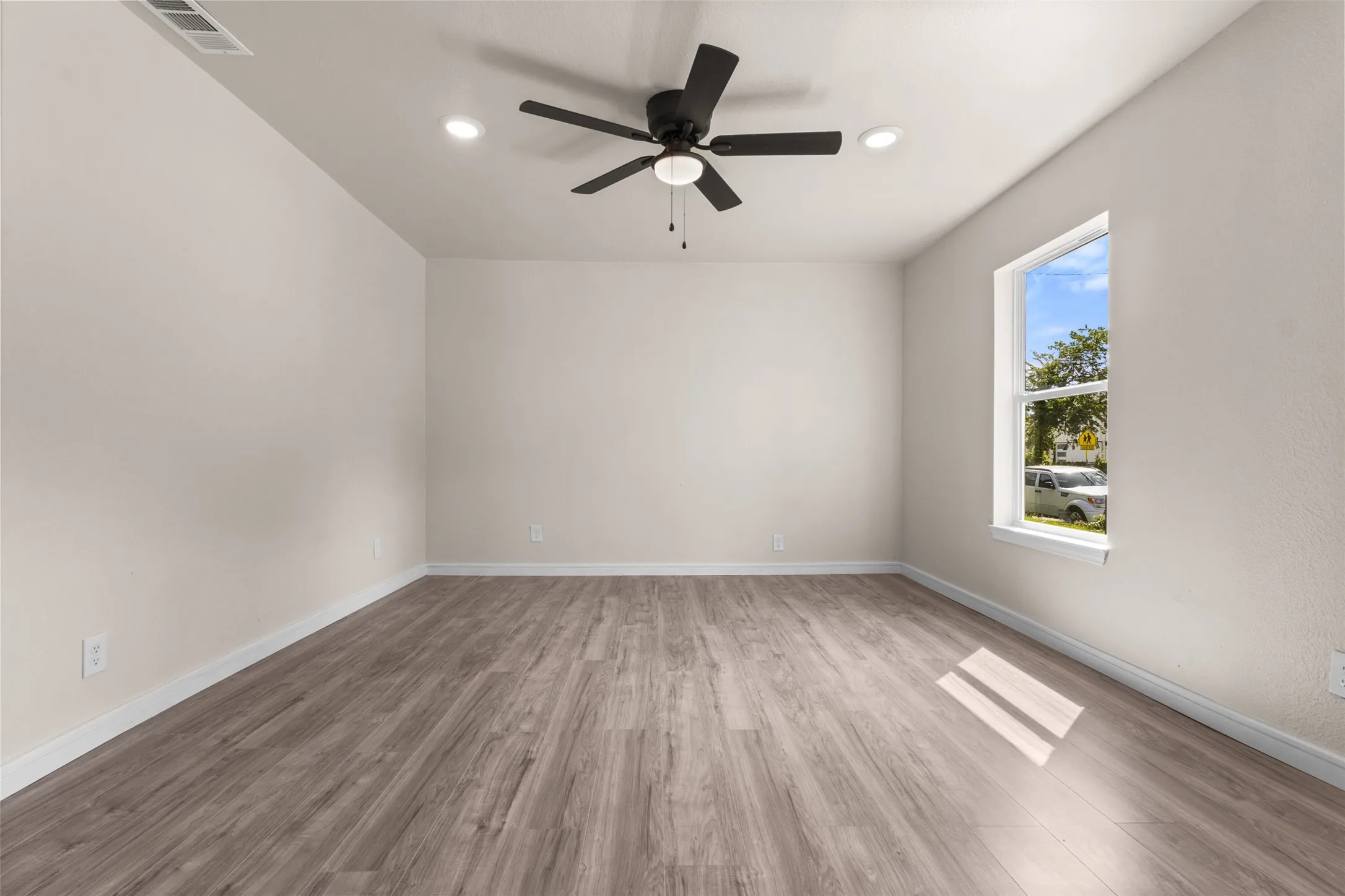 Spacious room featuring wood-finish flooring, light-colored walls, a ceiling fan, recessed lighting, and a large window