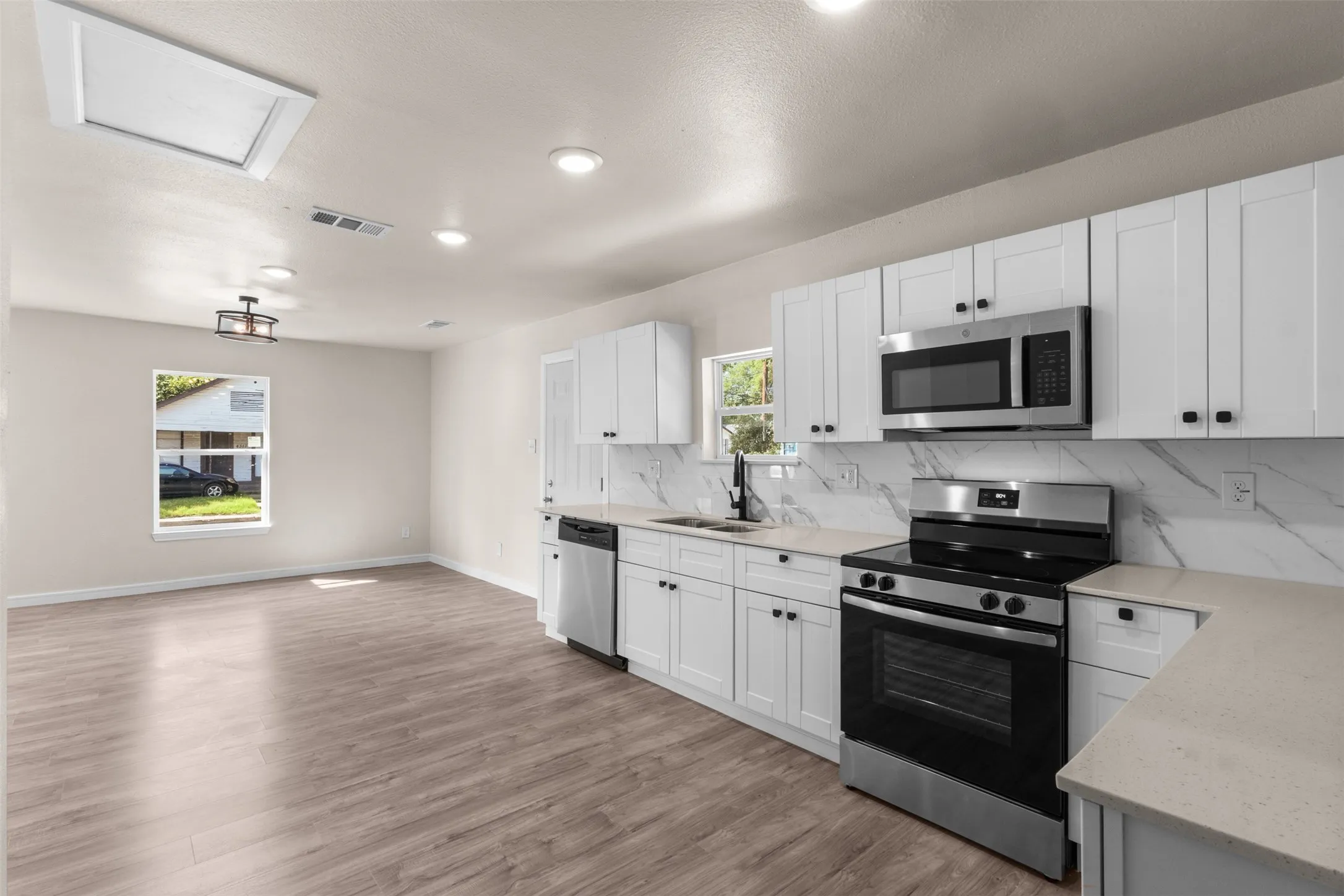Contemporary kitchen featuring white shaker cabinetry, stainless steel appliances, light countertops, and a full-height backsplash