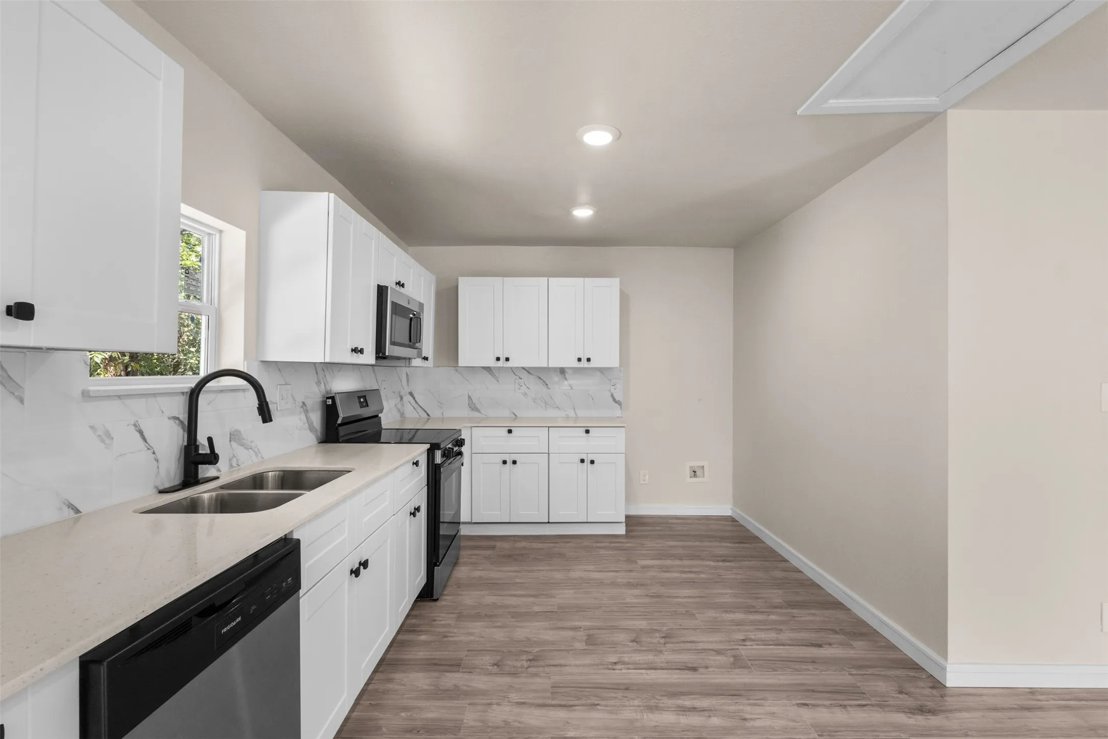 Contemporary kitchen featuring white cabinetry, light countertops, and a white and gray veined backsplash