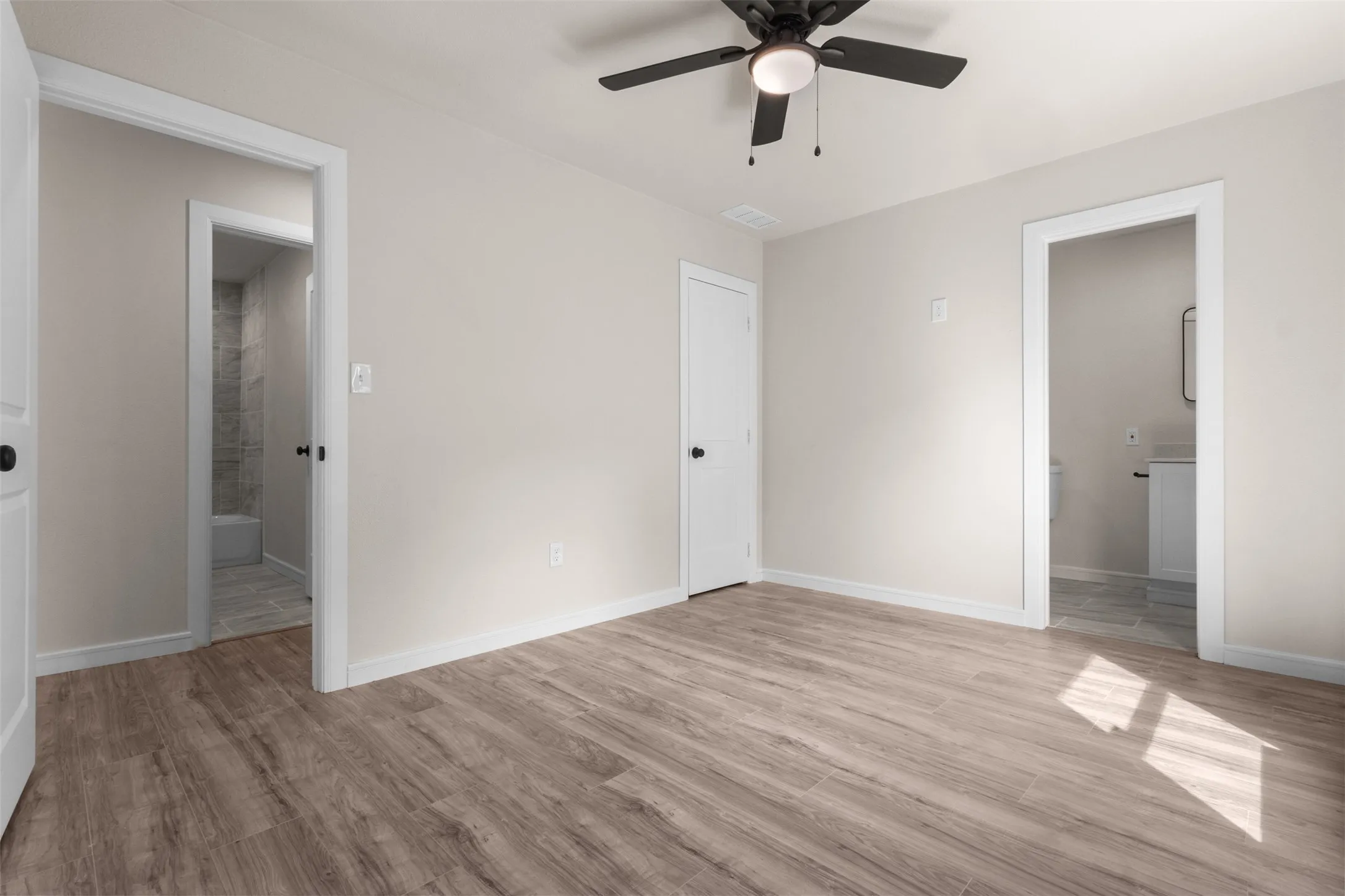 Spacious room featuring wood-finish flooring, light neutral wall paint, and a ceiling fan with integrated lighting