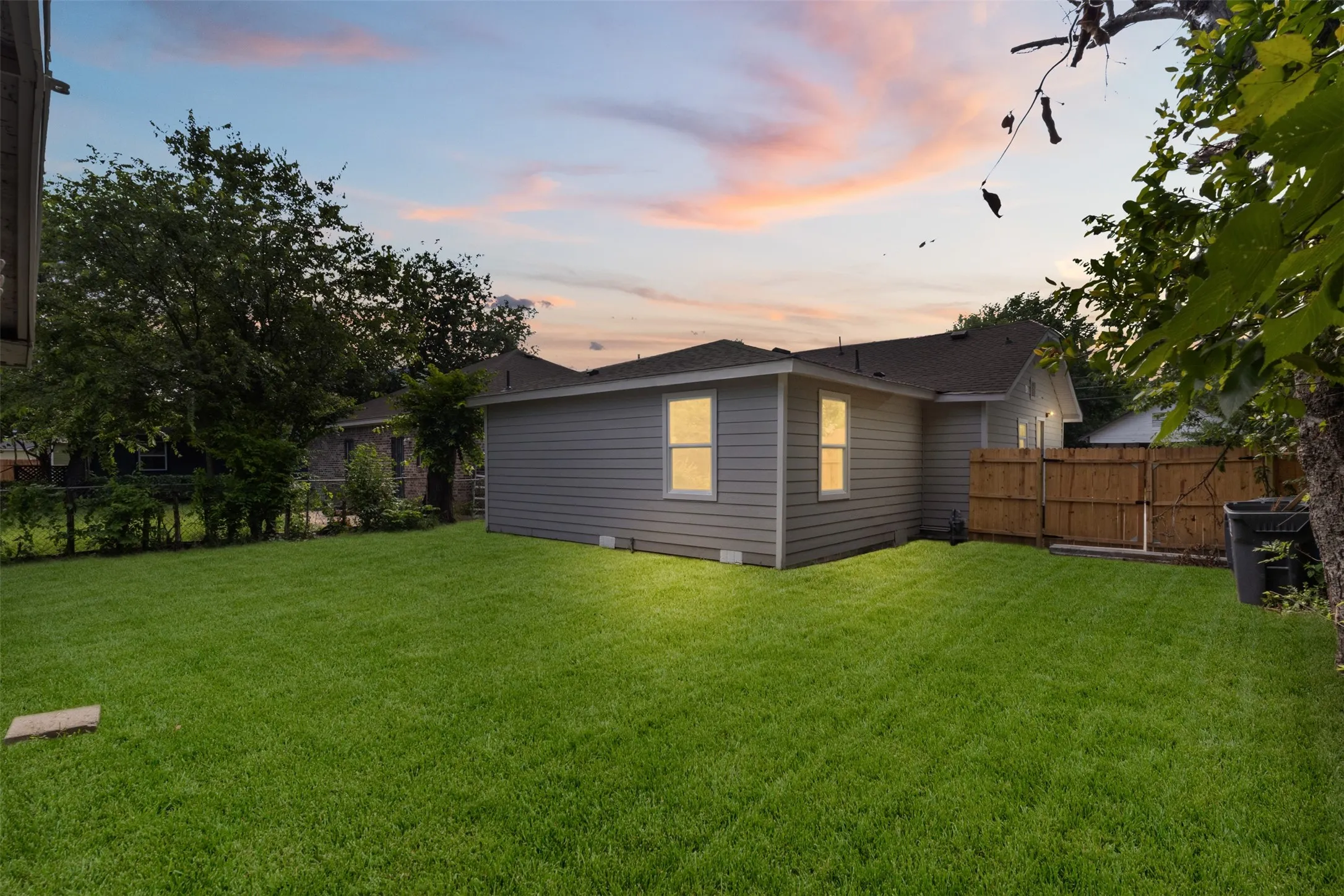 Expansive green lawn surrounds the property, featuring a gray siding exterior and multiple windows