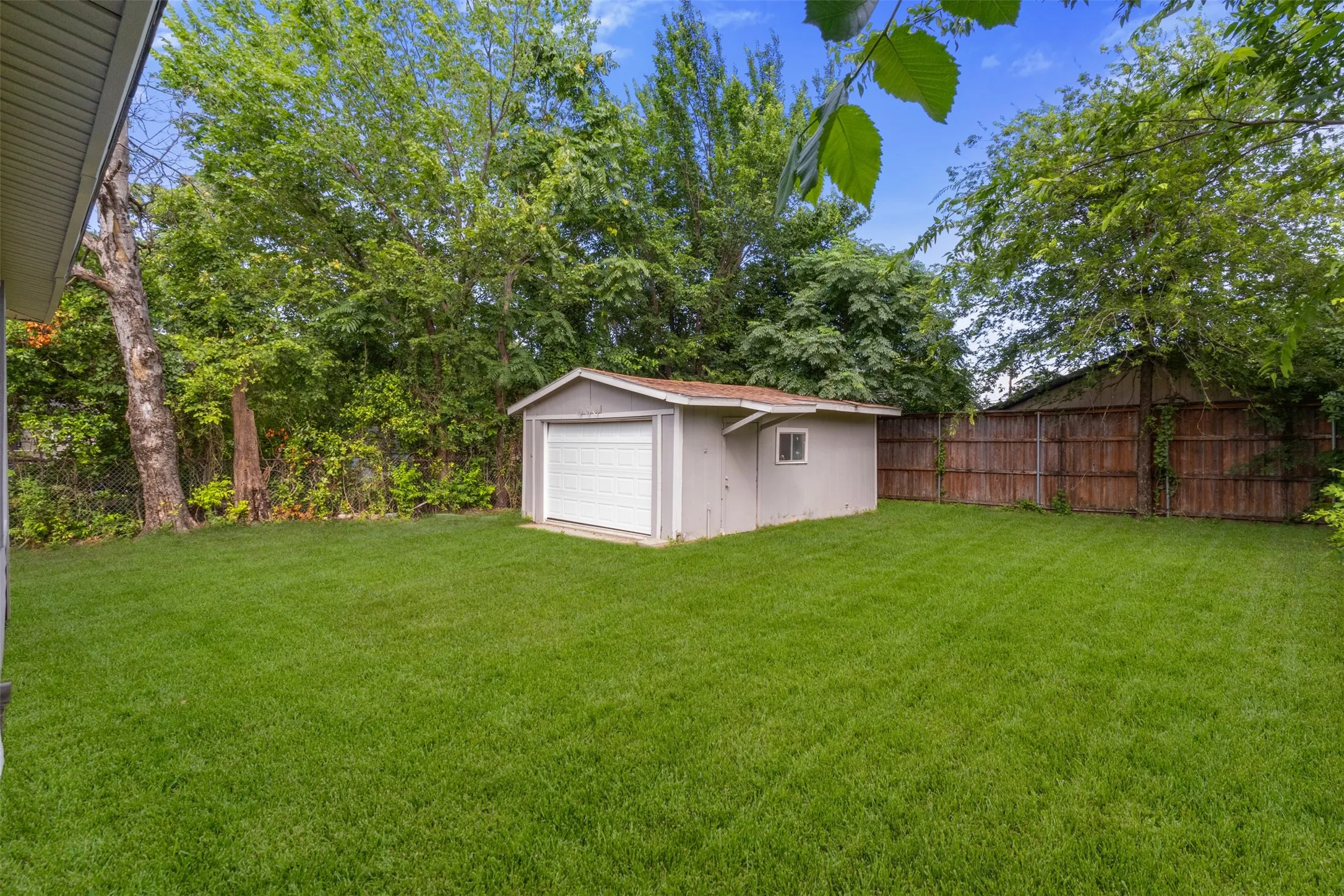 Expansive green lawn with a detached storage building featuring a roll-up garage door and side window