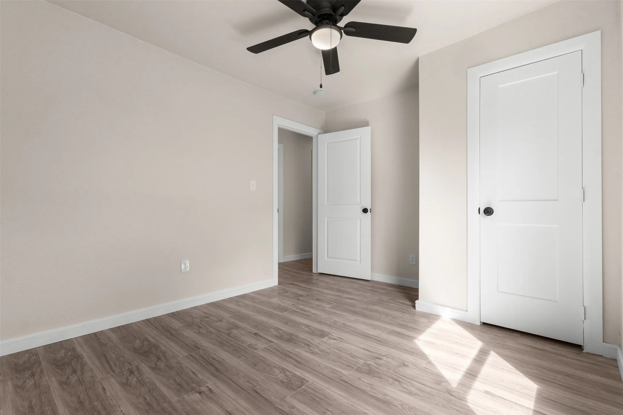 Open room featuring wood-finish flooring, light neutral wall paint, and white baseboards