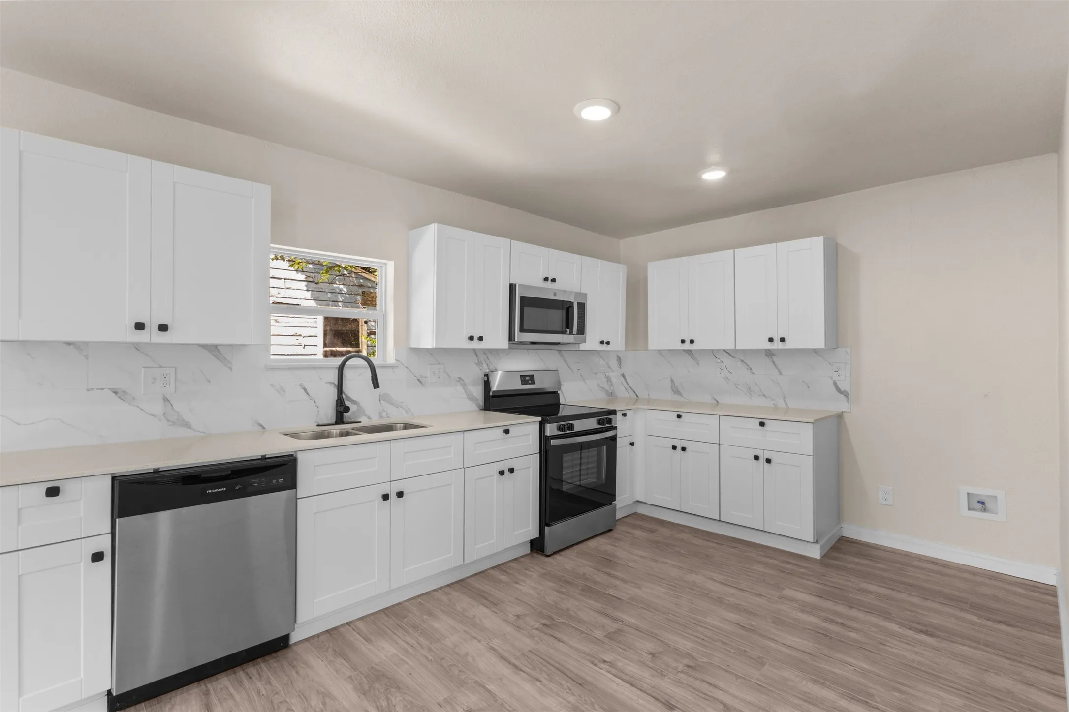 Modern kitchen featuring white shaker cabinetry, light-toned countertops, and a white marble-patterned backsplash