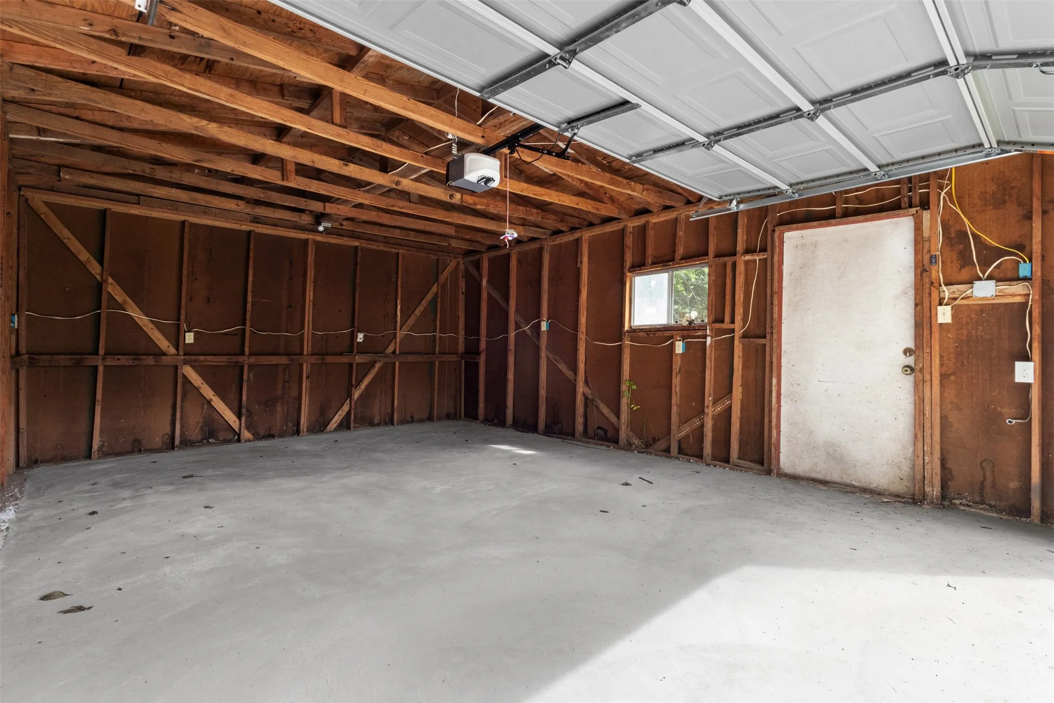 Spacious garage with exposed wood framing, concrete flooring, and a white overhead door