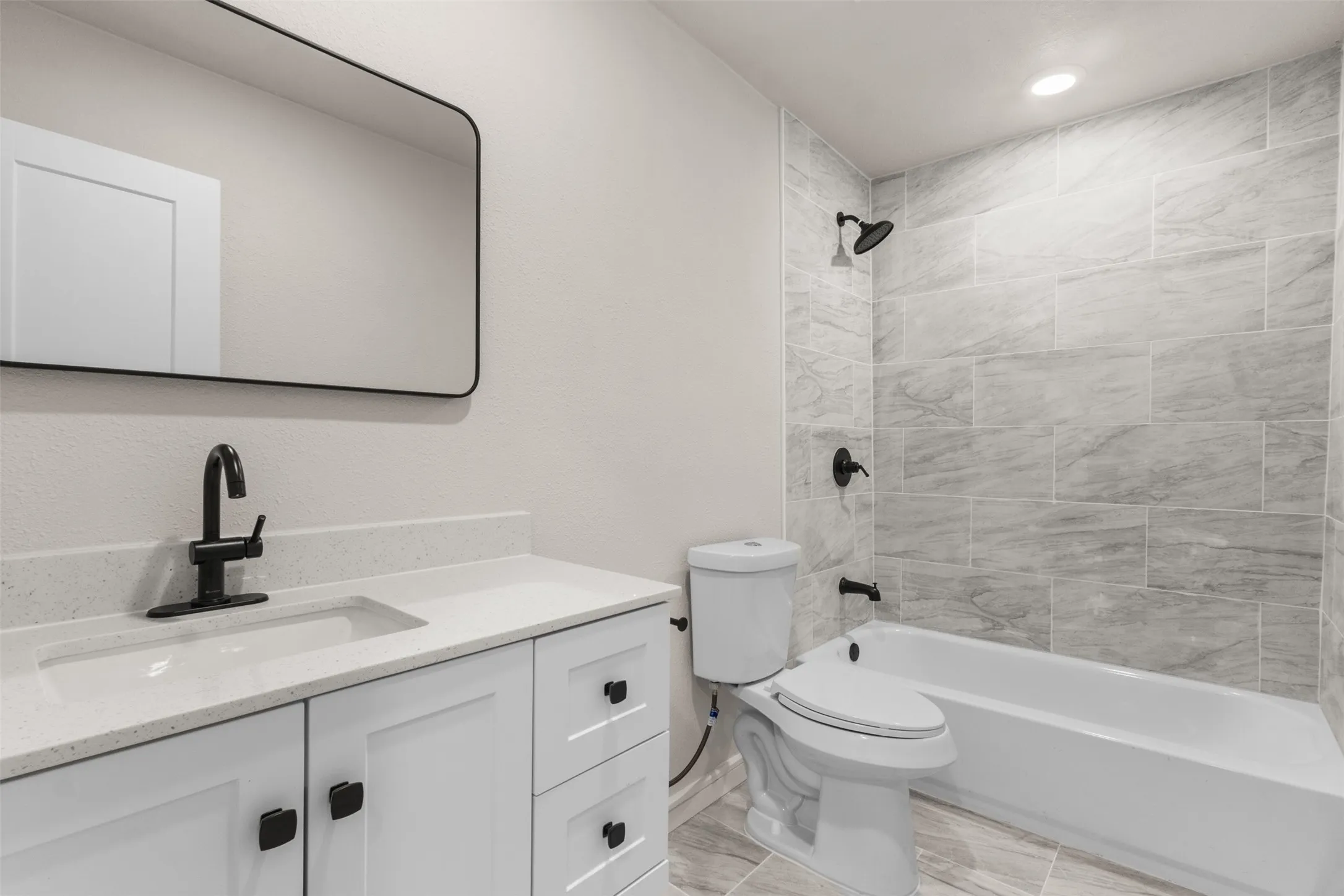 Bathroom featuring a white vanity with quartz countertop, integrated rectangular sink, matte black faucet, and a contemporary mirror