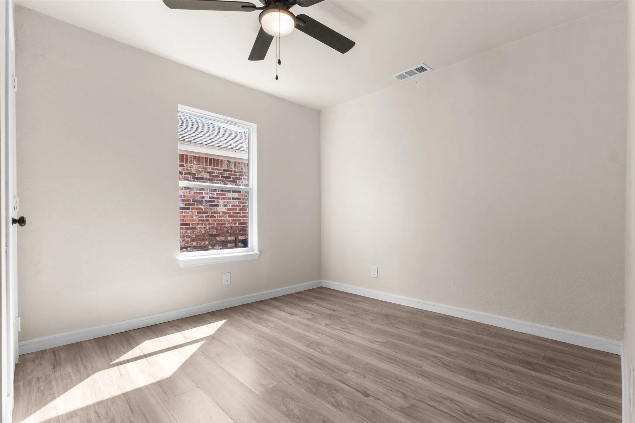Room featuring wood-finish flooring, a ceiling fan with integrated lighting, and a window with white trim