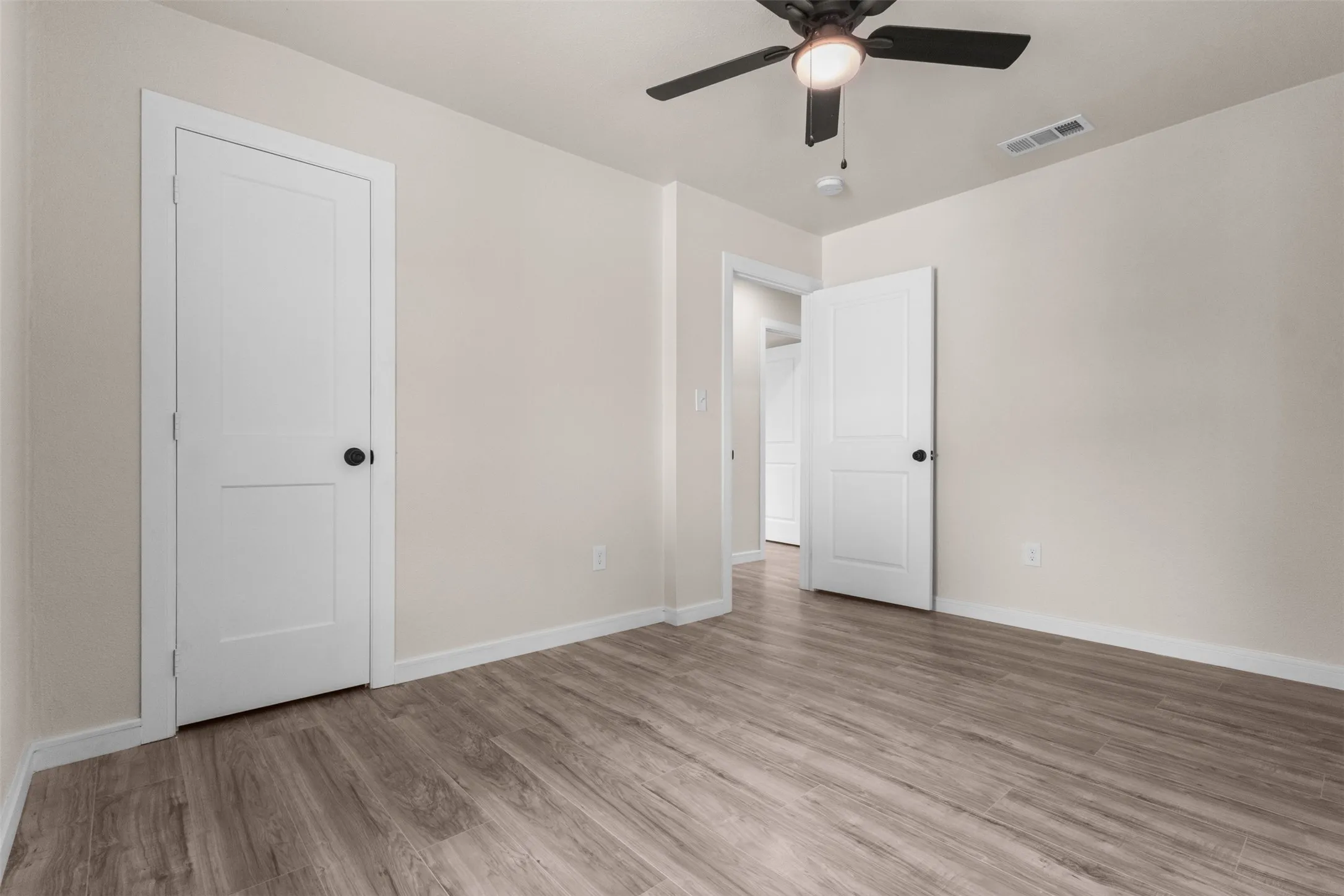 Interior room featuring wood-finish flooring, light neutral wall tones, white trim, and a ceiling fan with integrated lighting