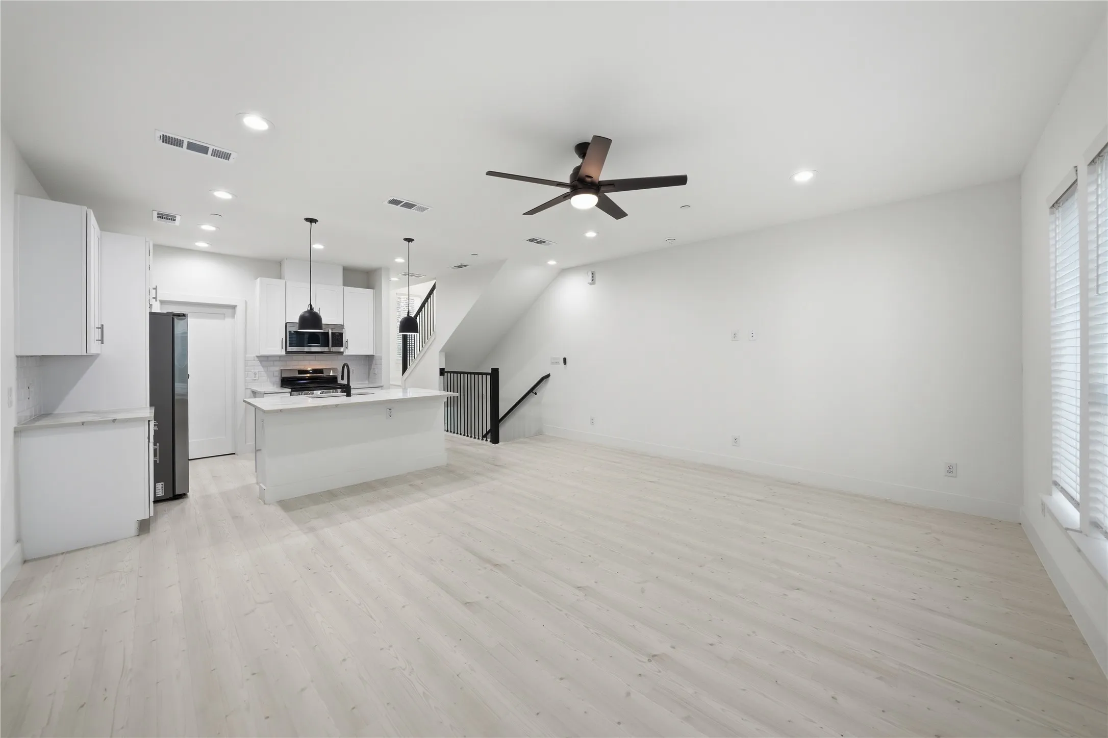 Open-concept living area with light wood-finish flooring, recessed lighting, and a modern ceiling fan