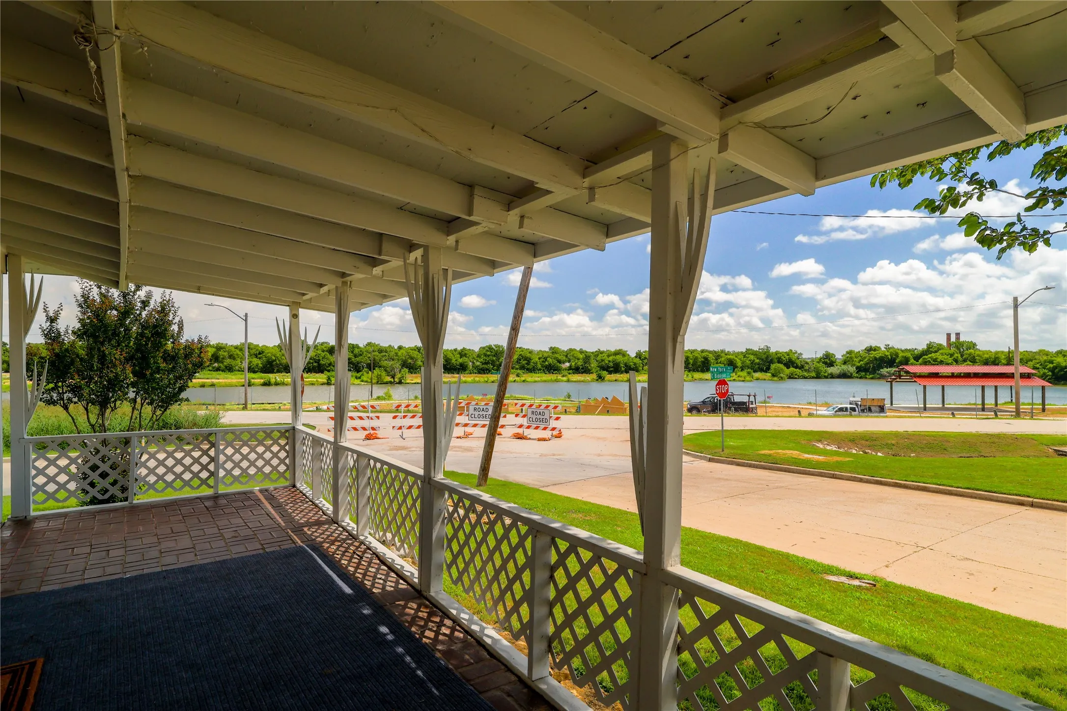 Covered porch featuring a lattice railing, brick-patterned flooring, and a water backdrop