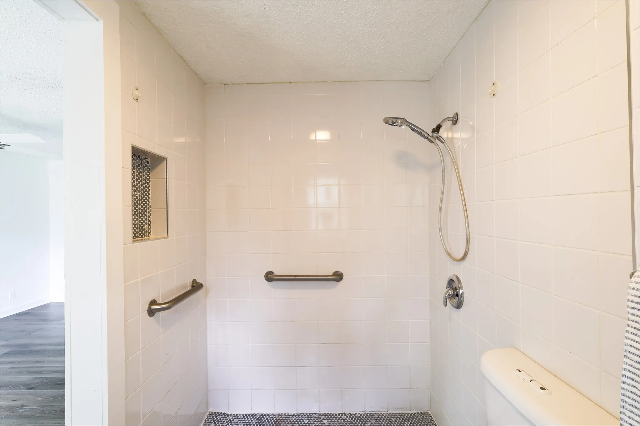 Tiled shower enclosure featuring a handheld showerhead, built-in bench, recessed niche, and grab bars