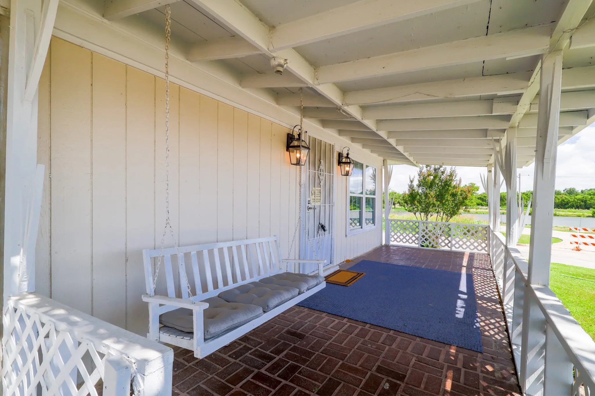 Covered front porch featuring brick flooring and white painted wood siding