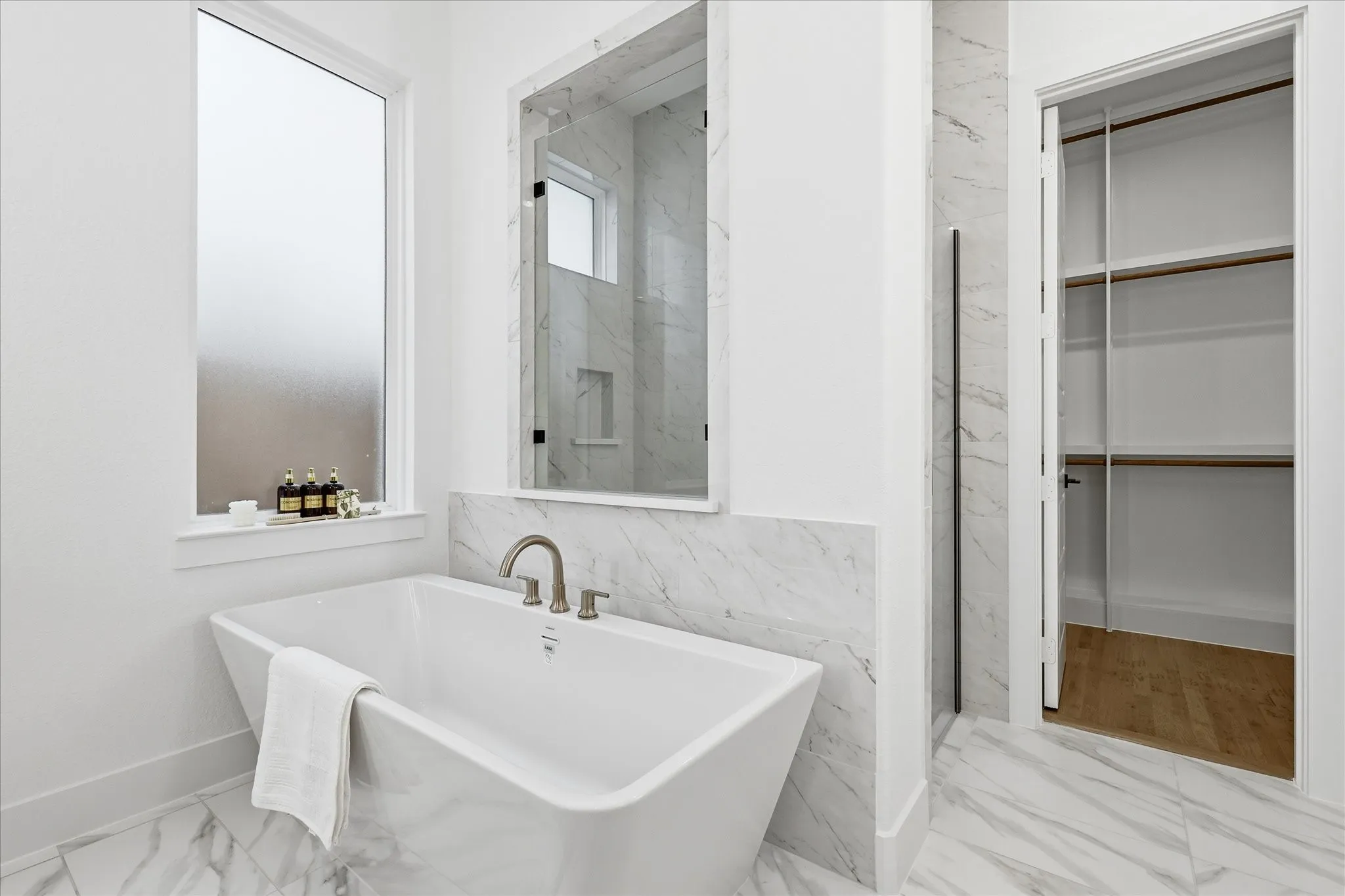 Freestanding soaking tub with brushed nickel fixtures, complemented by white and grey veined tile flooring and wainscoting
