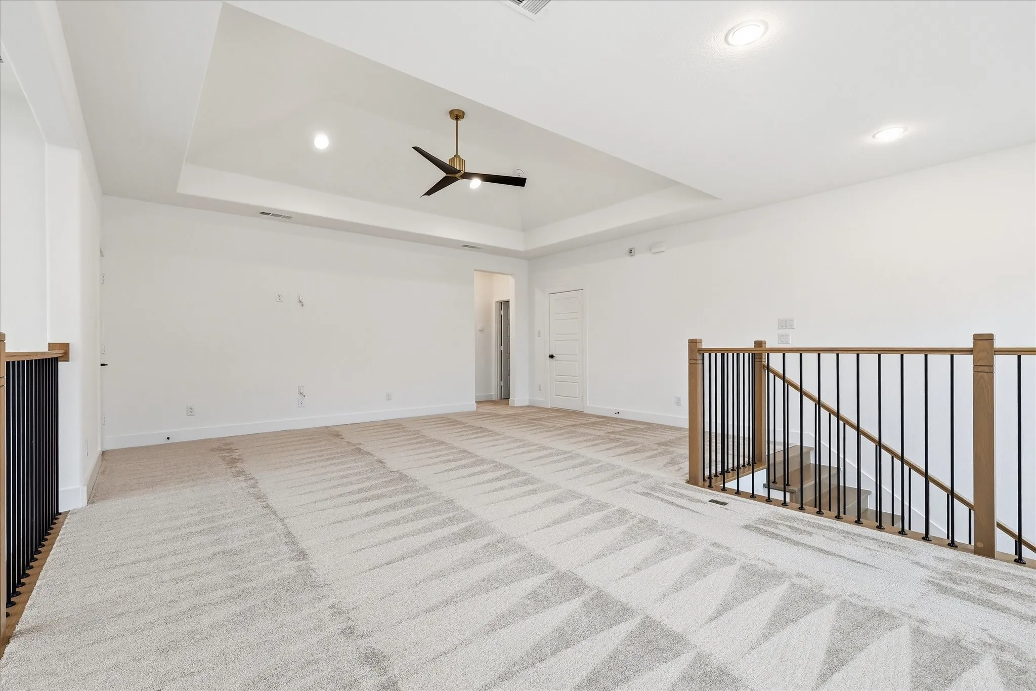 Spacious loft area featuring a tray ceiling with a modern ceiling fan, recessed lighting, and patterned carpeting