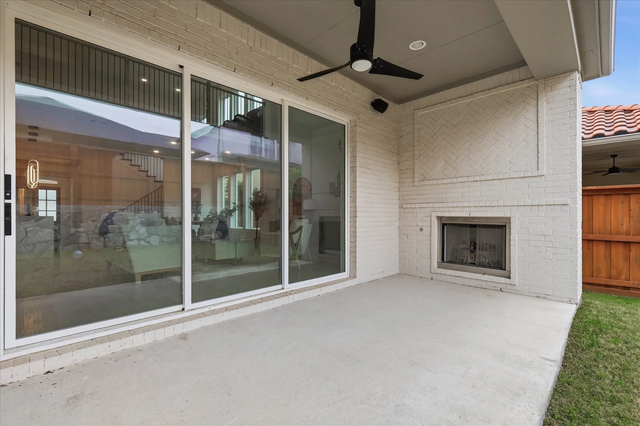 Covered outdoor patio featuring a built-in fireplace with a herringbone brick design, concrete flooring, and a ceiling fan