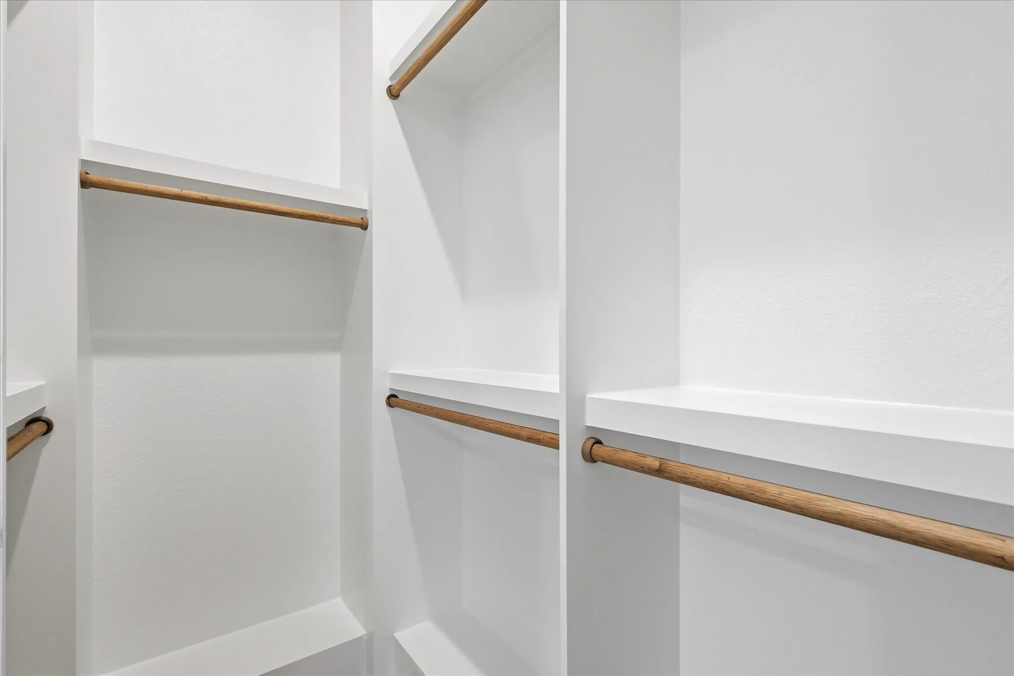 Built-in closet organization system featuring white cabinetry and light wood-finish rods