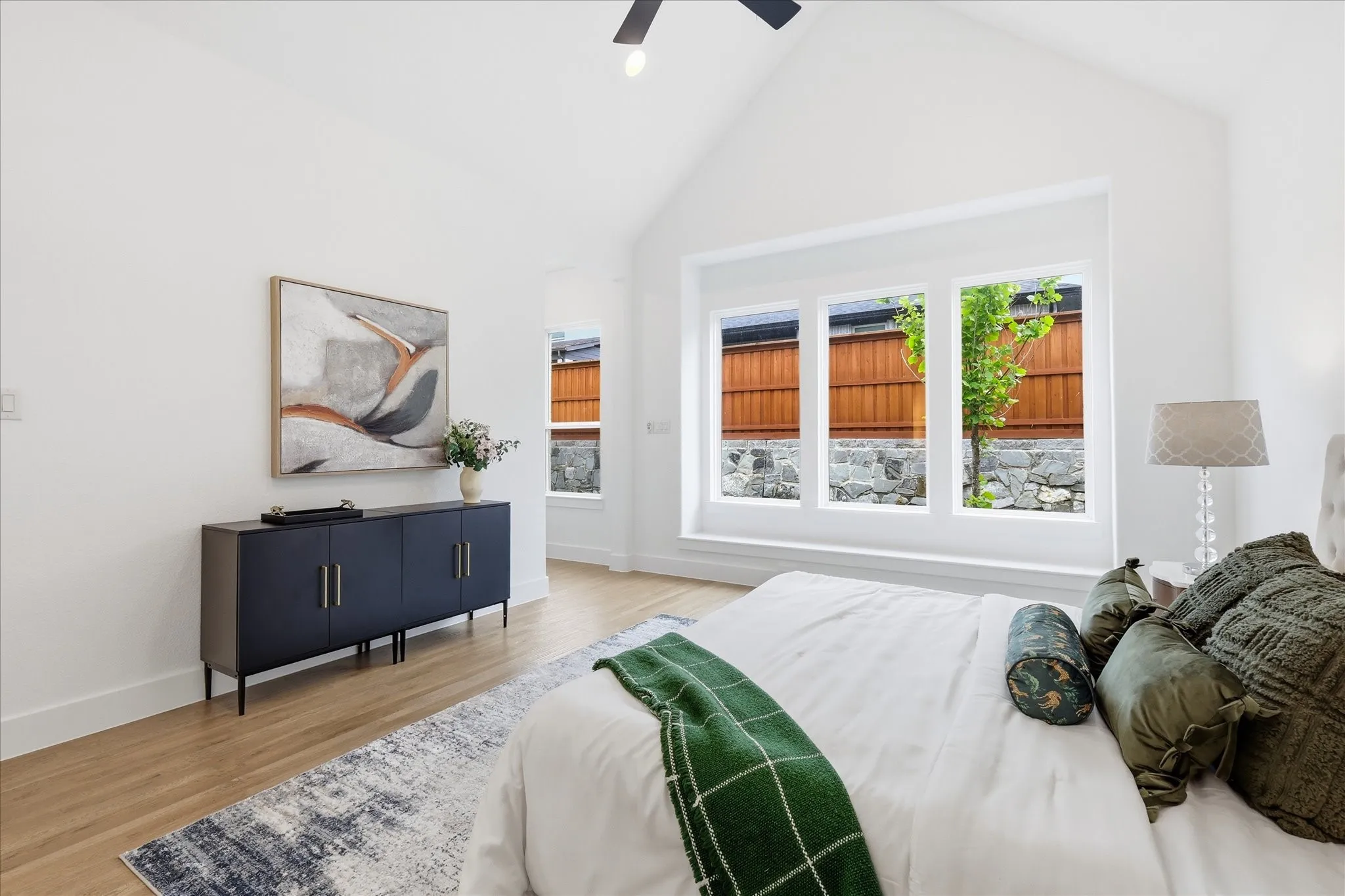 Vaulted ceiling with a ceiling fan, white walls, light wood-finish flooring, and a triple-pane window unit with a stone base