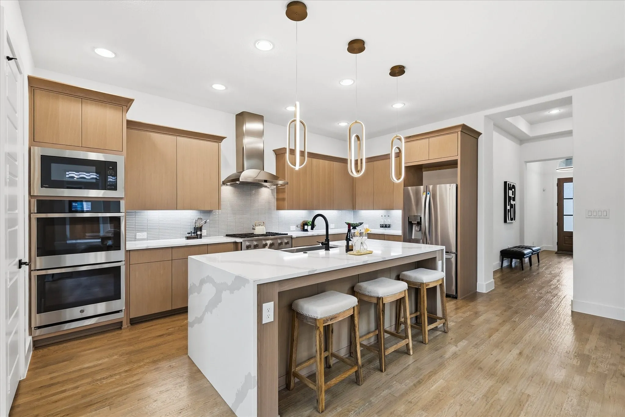 Contemporary kitchen featuring light wood-finish cabinetry, stainless steel appliances, a center island with a waterfall countertop, and pendant lighting fixtures