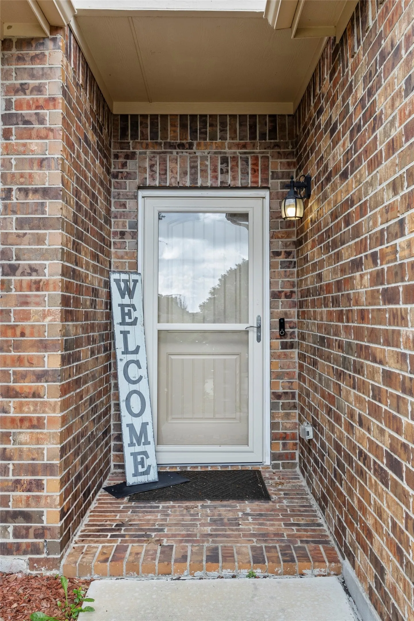 Brick entry with porch light fixture, security screen door, and concrete threshold