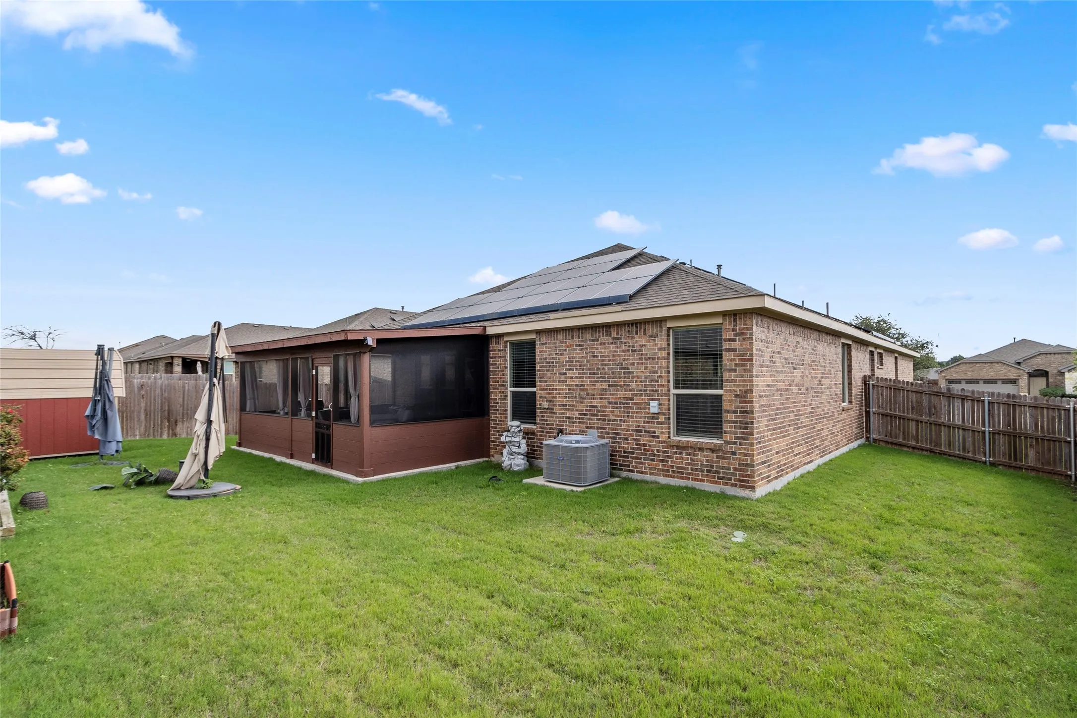 Expansive backyard featuring a screened-in patio, brick exterior, solar panels, and wood fencing
