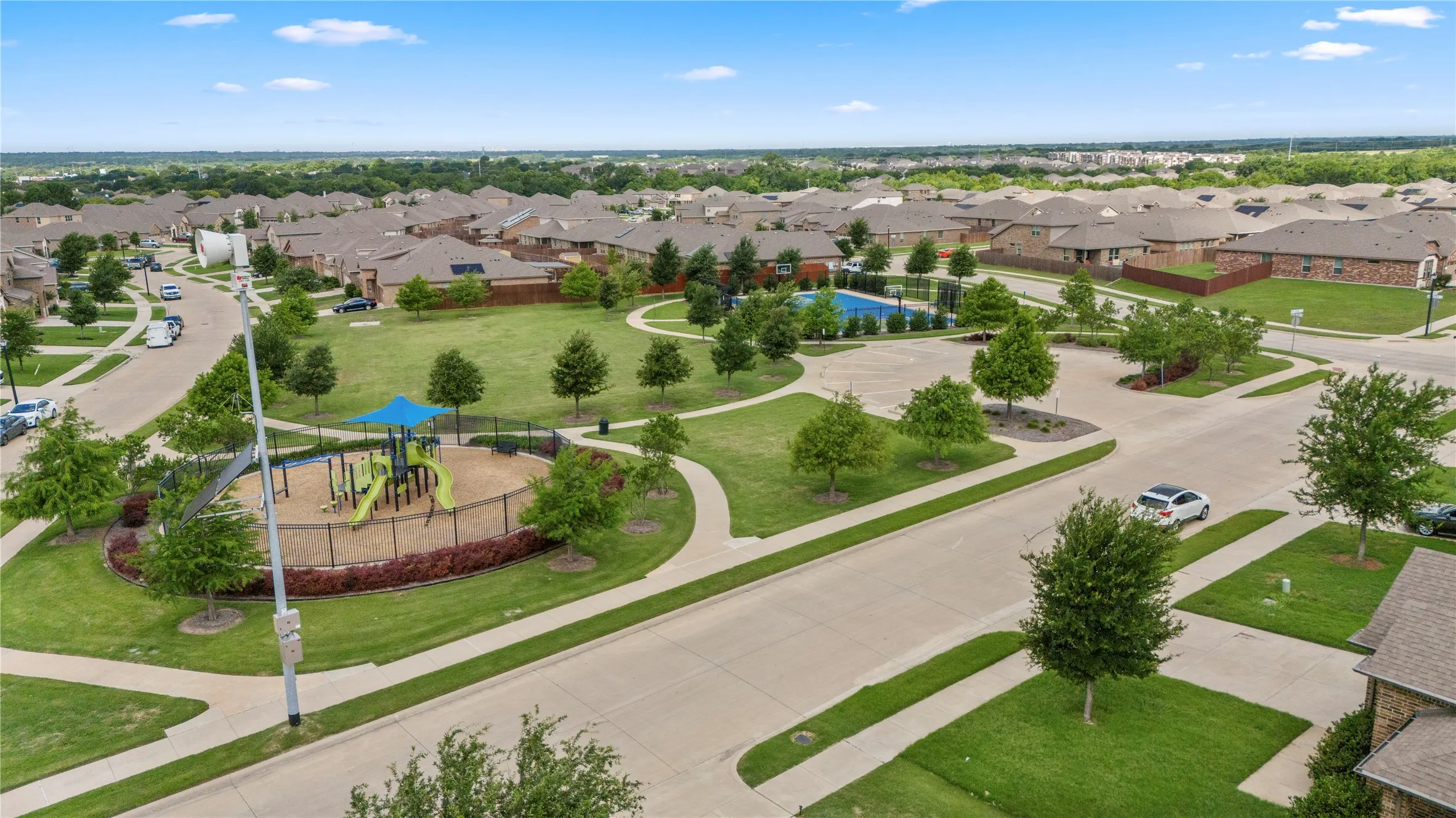 Aerial view showcasing a neighborhood green space with a playground, mature trees, and a community swimming pool