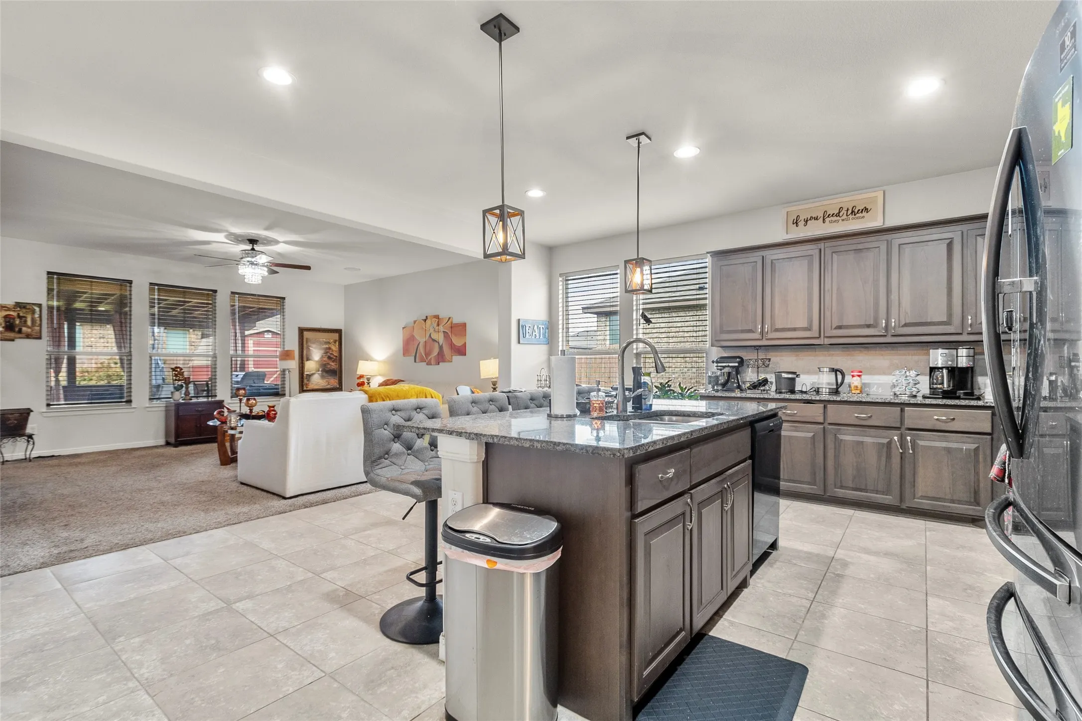 Open-concept kitchen featuring an island with a sink and pendant lighting, grey cabinetry, dark countertops, and tile flooring