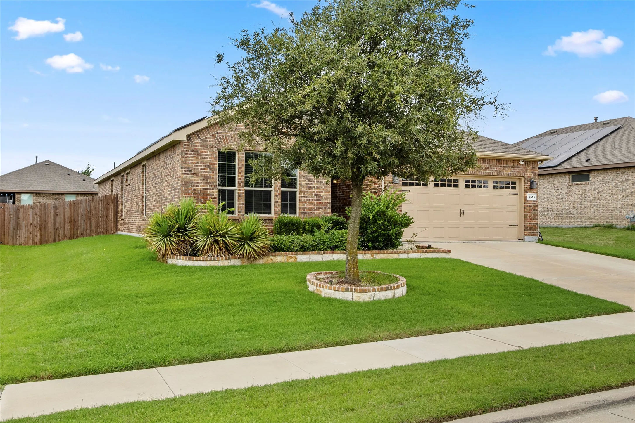 Brick exterior featuring a two-car garage, concrete driveway, and a front yard with mature landscaping