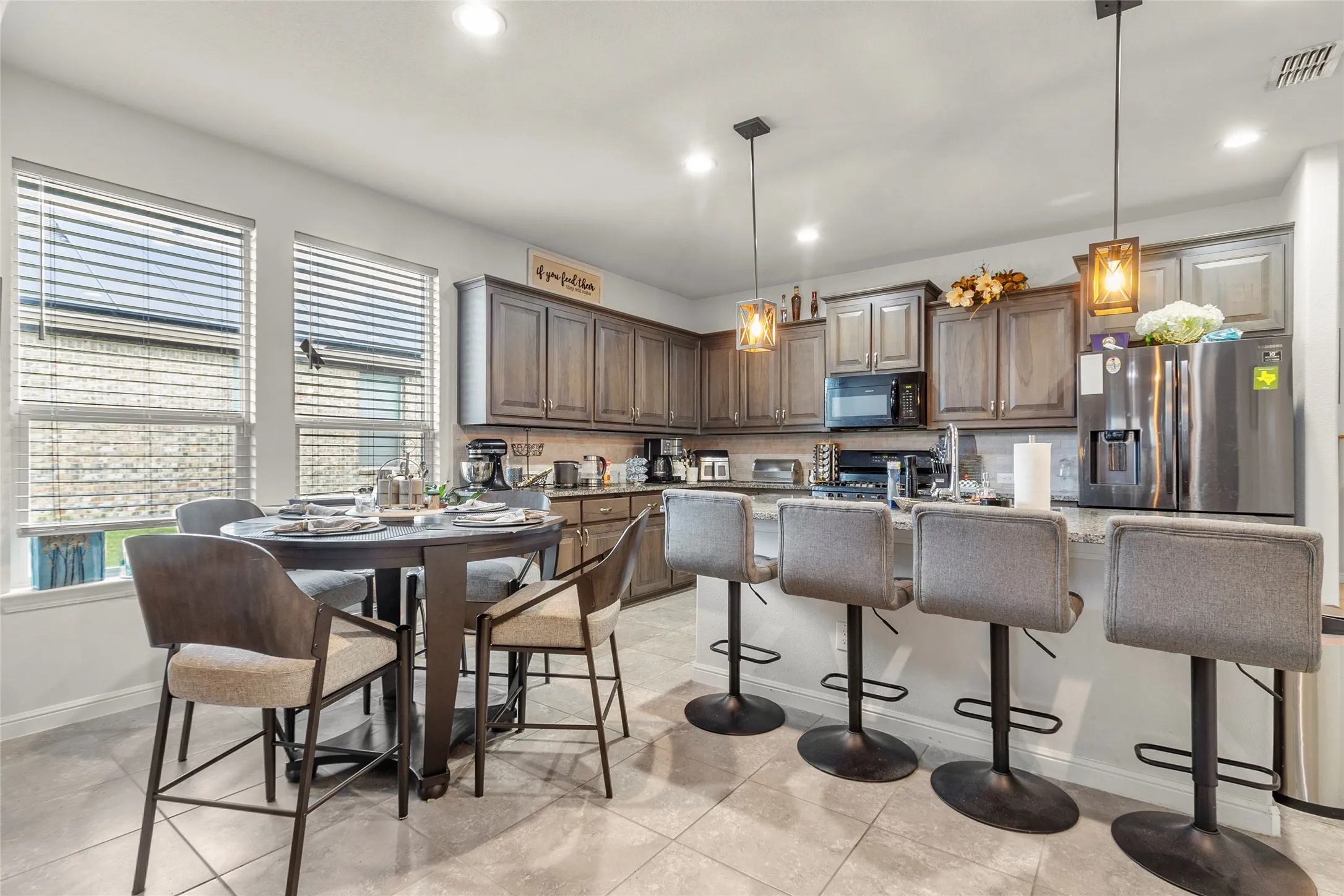 Well-appointed kitchen featuring granite countertops, wood-finish cabinetry, stainless steel refrigerator, built-in microwave, and pendant lighting
