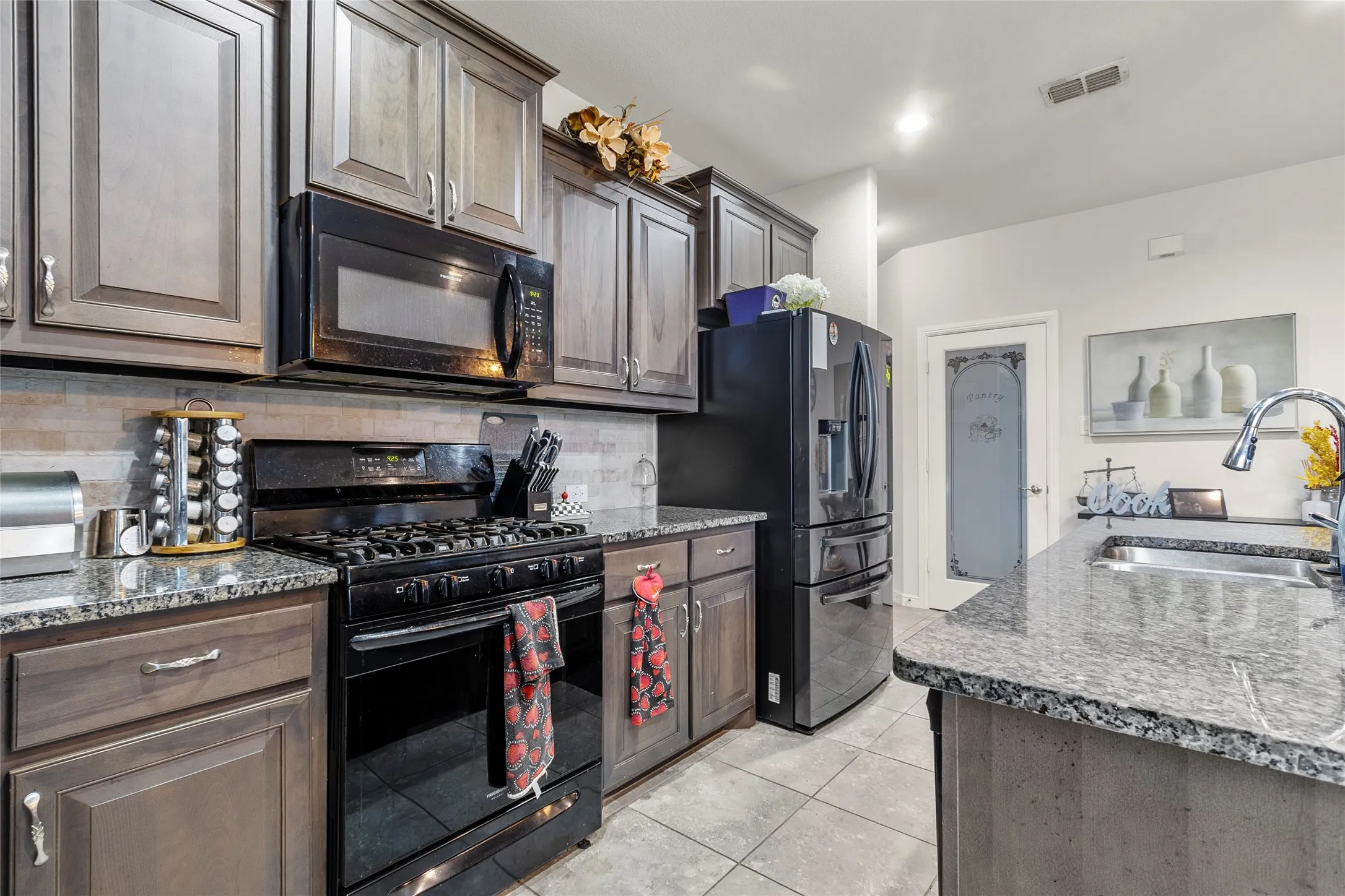 Kitchen featuring granite countertops, wood-finish cabinetry, black gas range, built-in microwave, and tile flooring