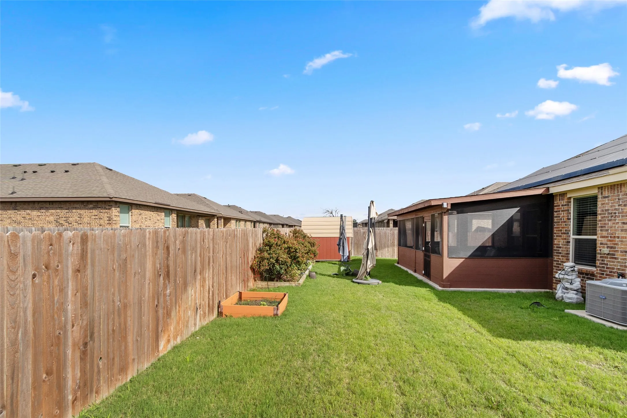 Expansive green lawn featuring a wooden privacy fence, a screened-in patio, and a raised garden bed