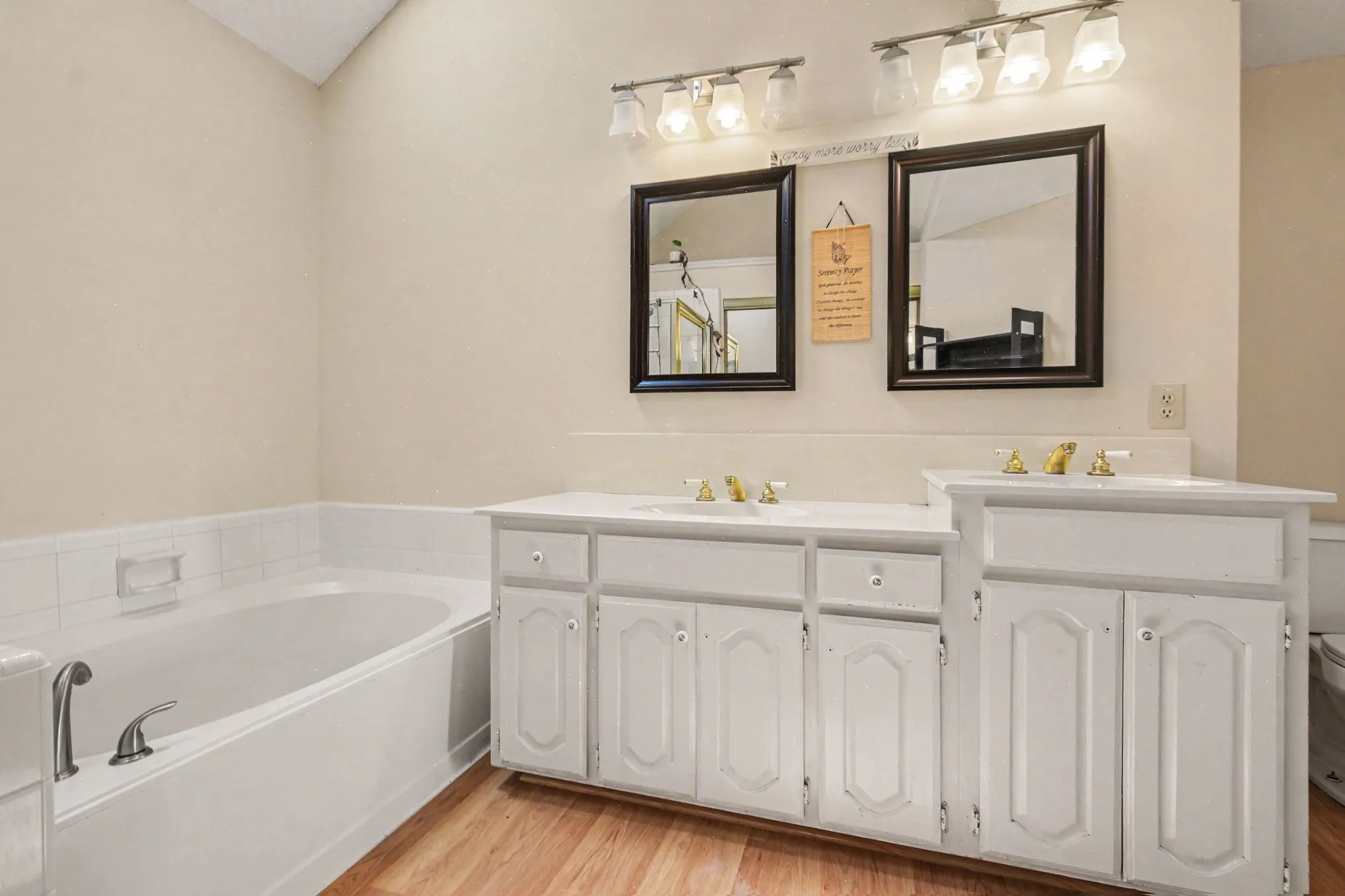 Bathroom featuring a soaking tub, dual vanity with white cabinetry, light-toned walls, wood-finish flooring, and overhead lighting fixtures