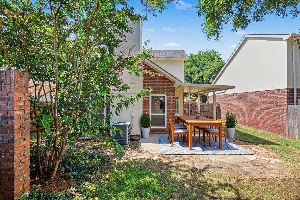 Virtually staged backyard patio area featuring a covered awning, concrete and flagstone surfacing, and mature landscaping