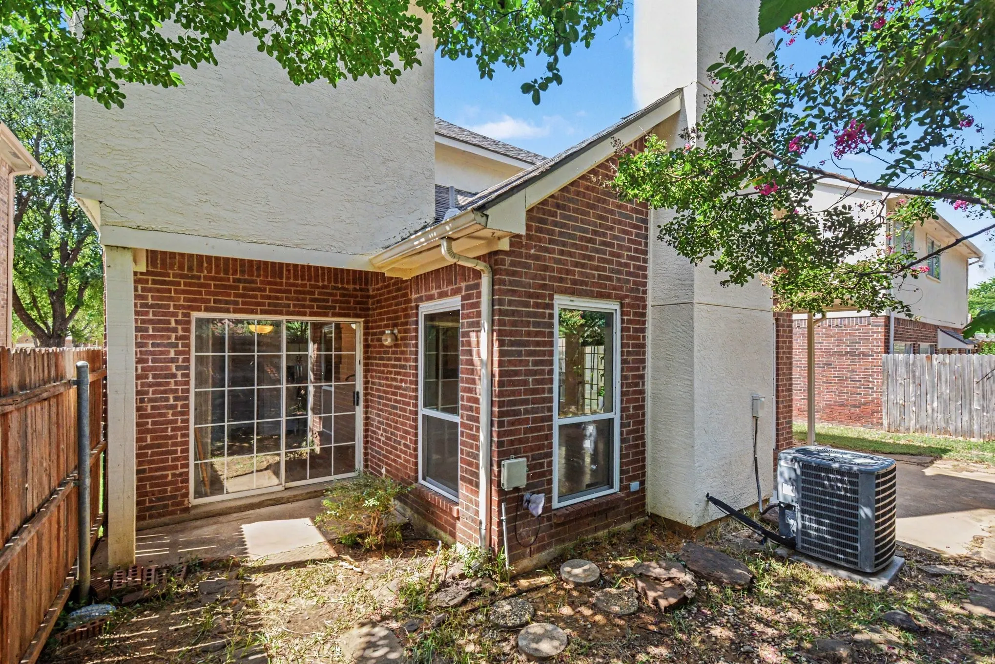 Brick exterior featuring a sliding glass patio door, multiple windows, and a privacy fence