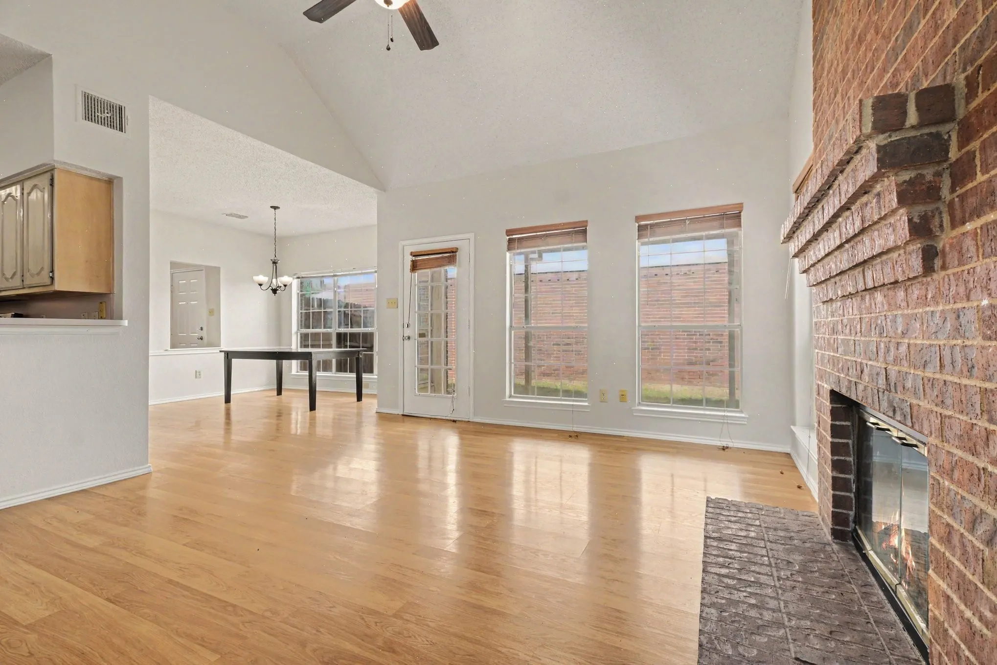 Vaulted living room featuring wood-finish flooring, a brick-surround fireplace with hearth, and a ceiling fan