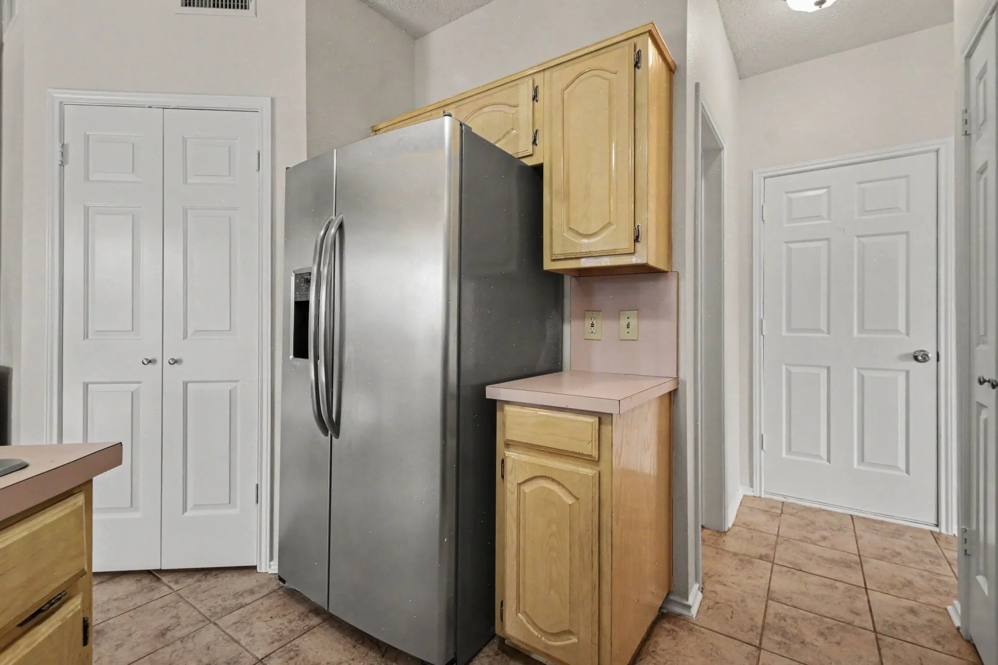 Stainless steel side-by-side refrigerator, light wood-finish cabinetry, and ceramic tile flooring