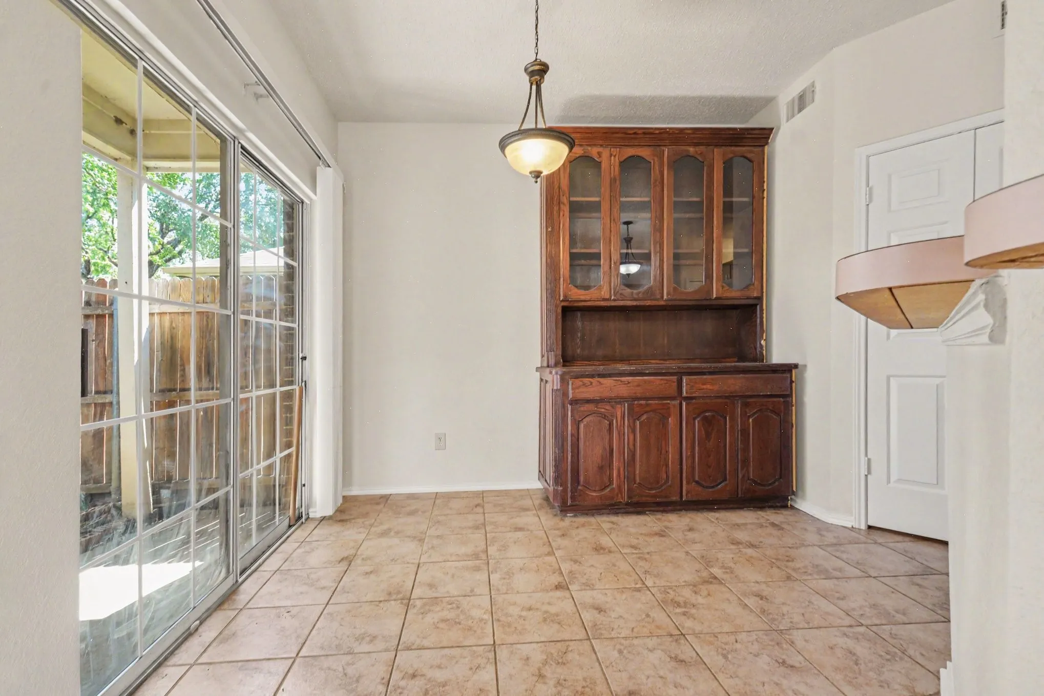 Additional dining area featuring ceramic tile flooring, a wood-finish hutch with glass-front cabinetry, a decorative pendant light fixture, and sliding glass doors with grid patterns opening to an outdoor area
