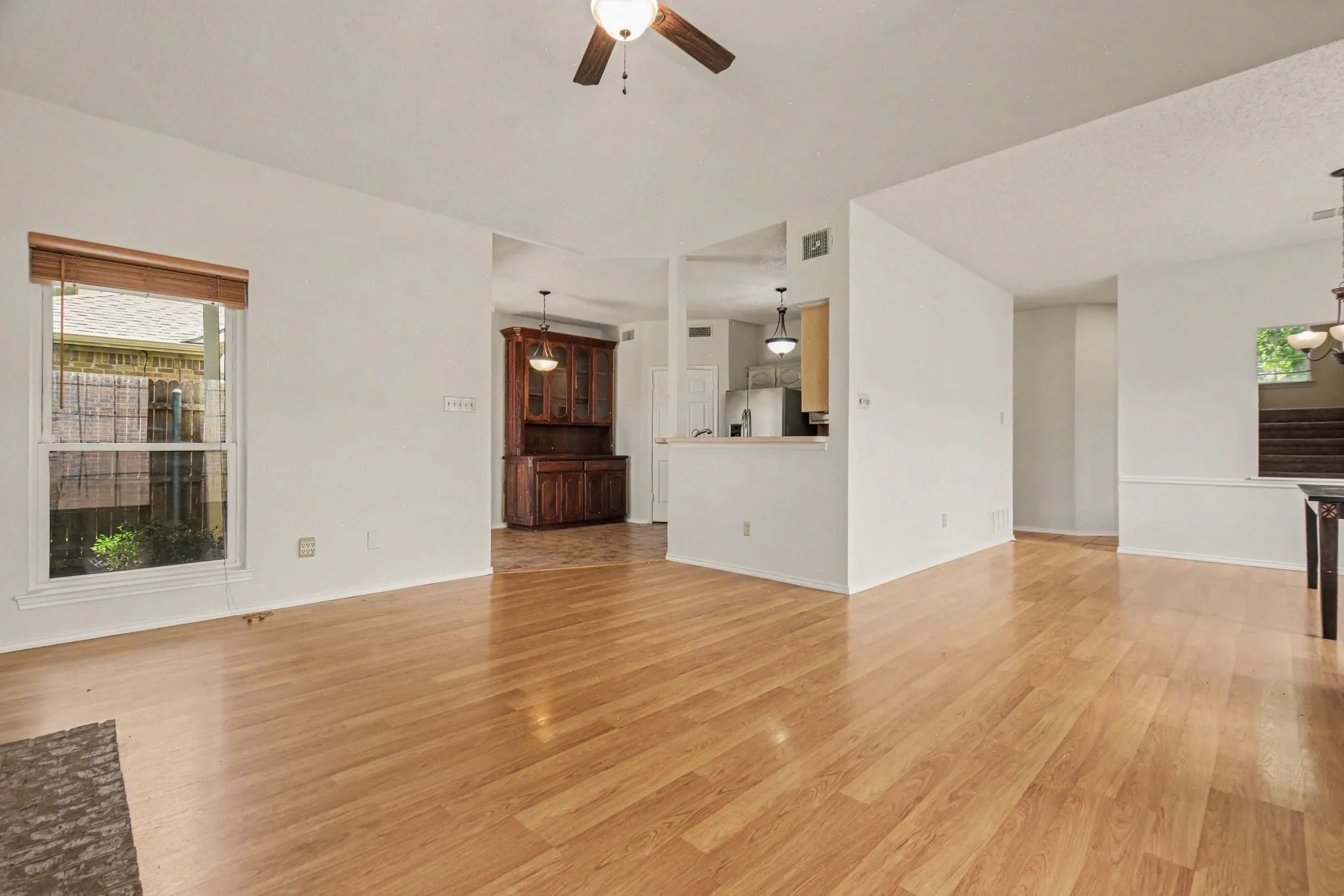 Freshly painted, spacious living room with open floorplan, area featuring wood-finish flooring, a ceiling fan with integrated lighting, and a double-pane window with wood blinds