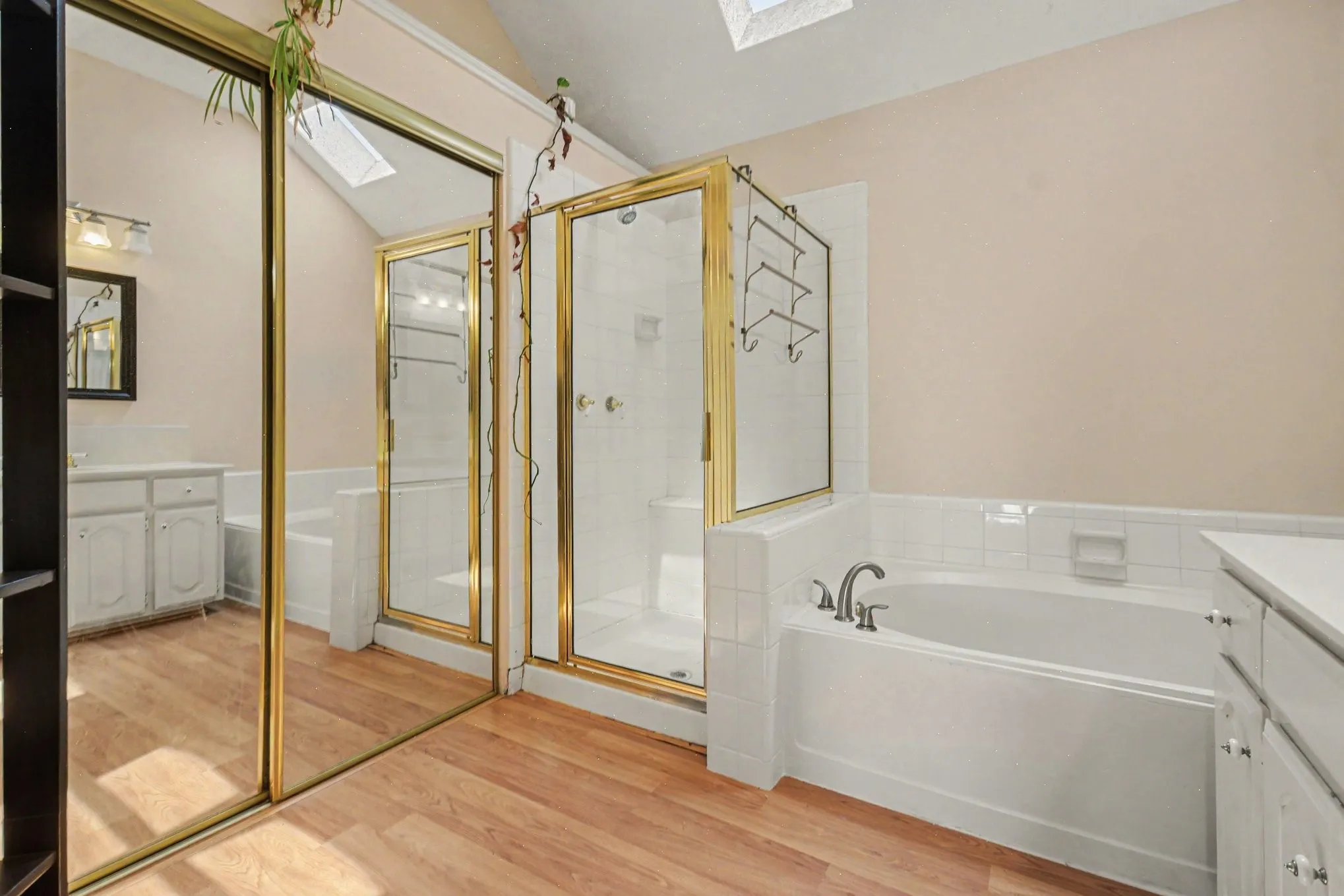 Bathroom featuring a built-in bathtub, a walk-in shower with gold-framed glass enclosure, and wood-finish flooring
