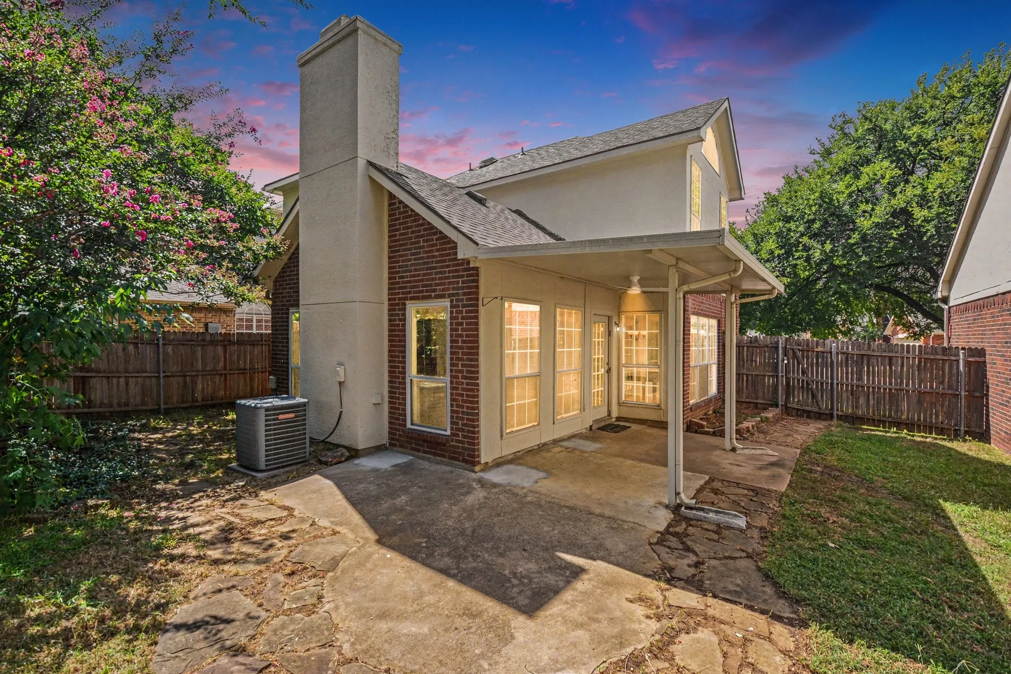 Rear exterior featuring a covered patio, brick and stucco siding, a tall chimney, and multiple large windows