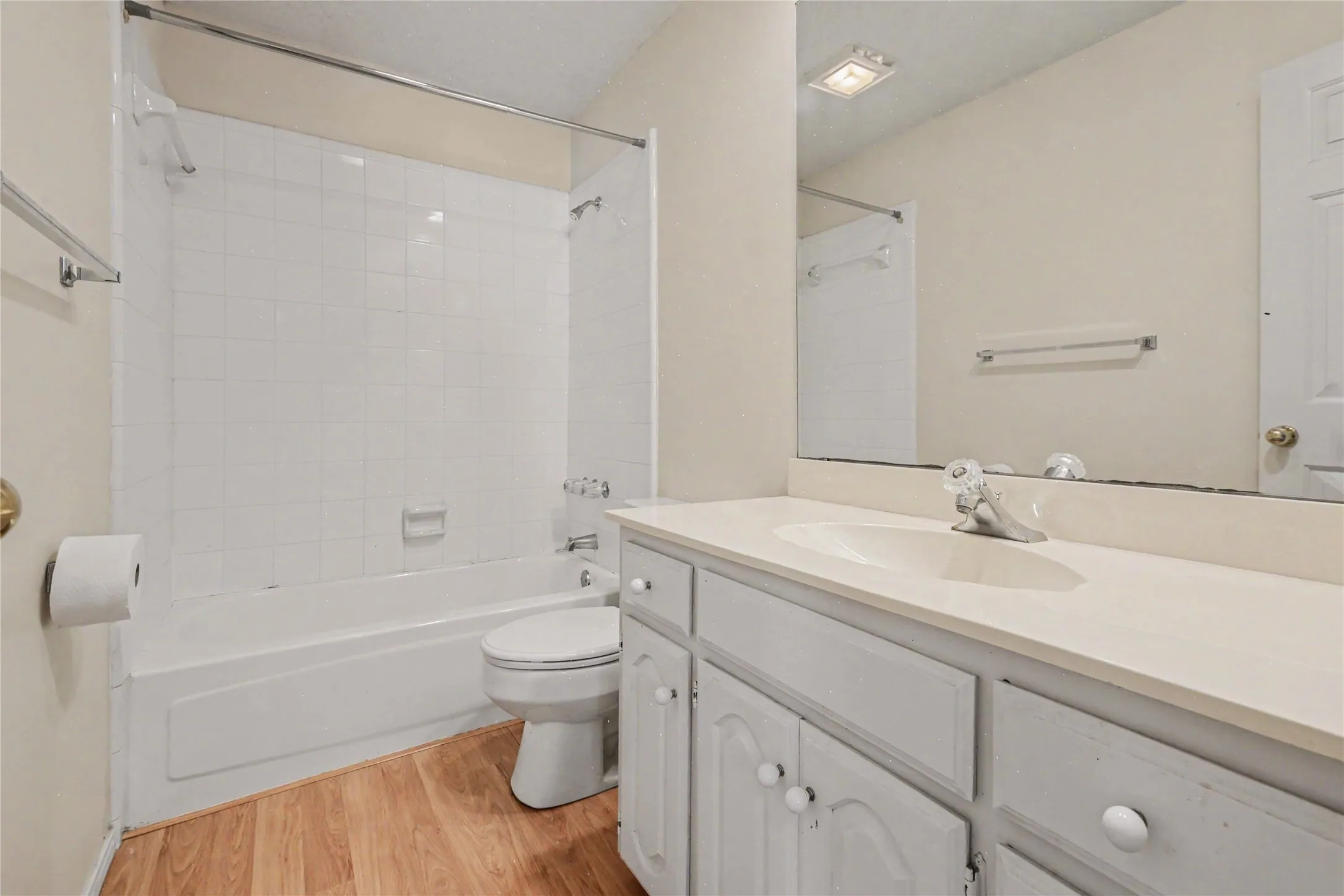 2nd full bathroom, featuring a white bathtub, white tiled shower surround, light wood-finish flooring, and a vanity with a white countertop and white cabinetry