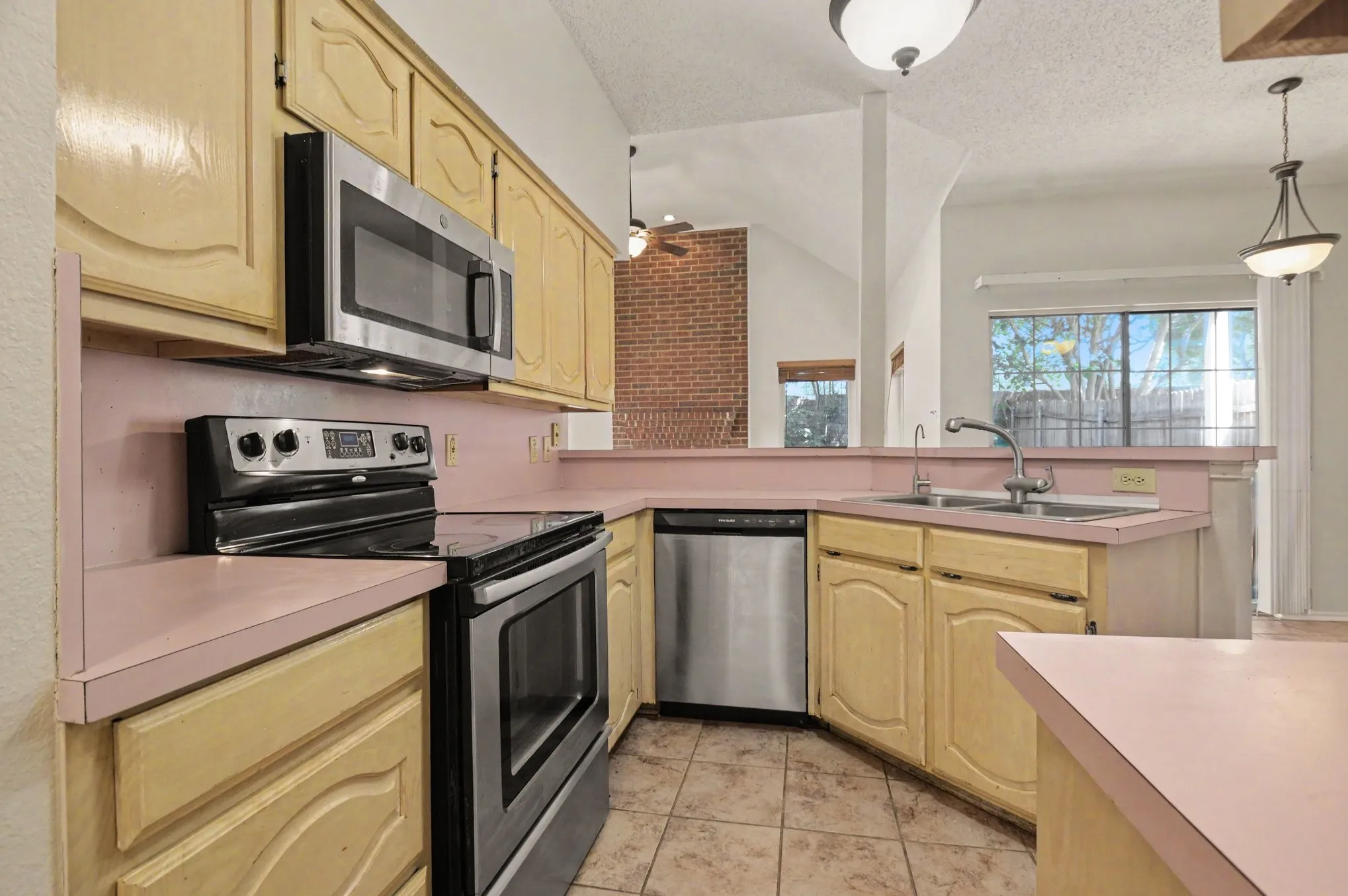 Kitchen featuring light-toned cabinetry, stainless steel appliances, a dual-basin sink, tiled flooring, and an integrated microwave