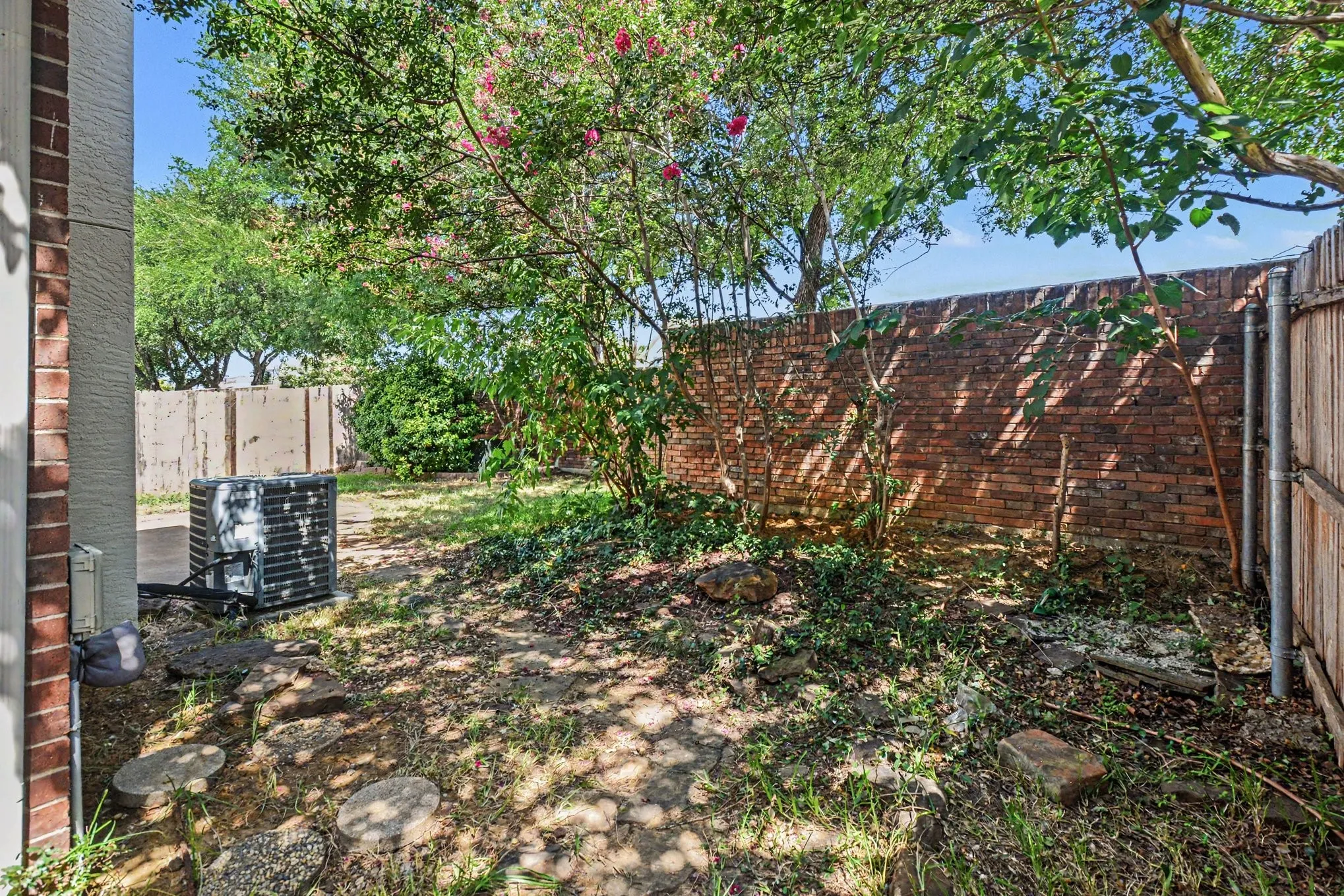 Dog, children, guests can enjoy the private yard space featuring a brick privacy wall, established trees, and stepping stones